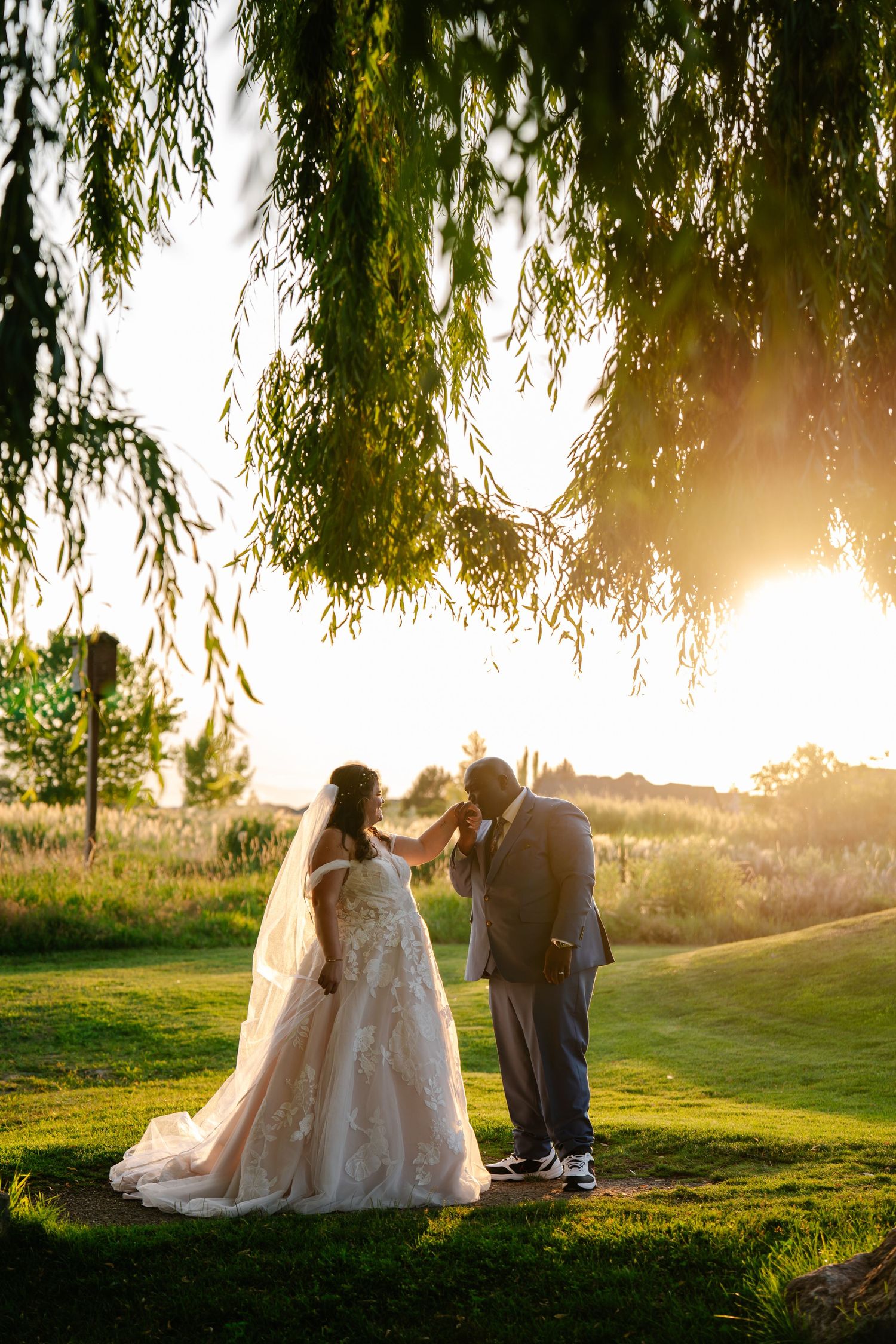 A romantic wedding moment captured at sunset under a weeping willow tree on a golf course.