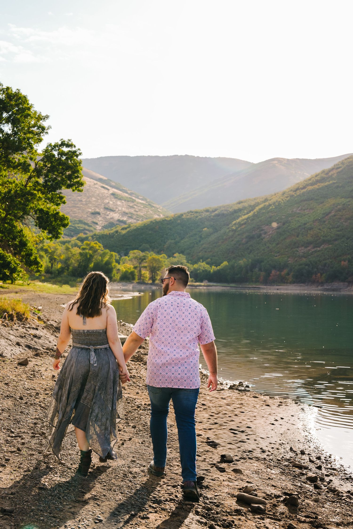 Two people explore a scenic mountain lake shoreline at sunset.