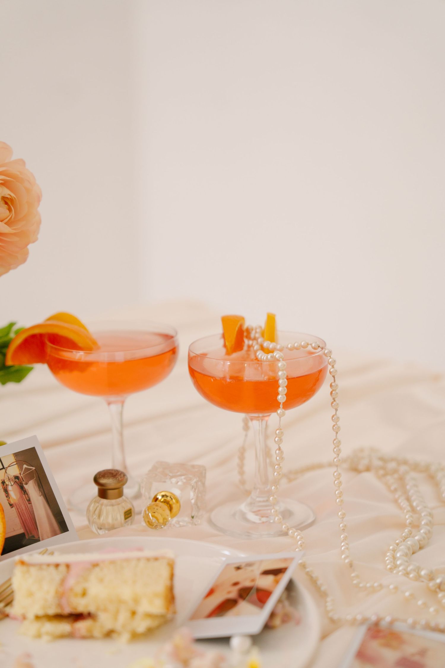 Orange cocktails and pearls arranged elegantly on a table with dessert plates.