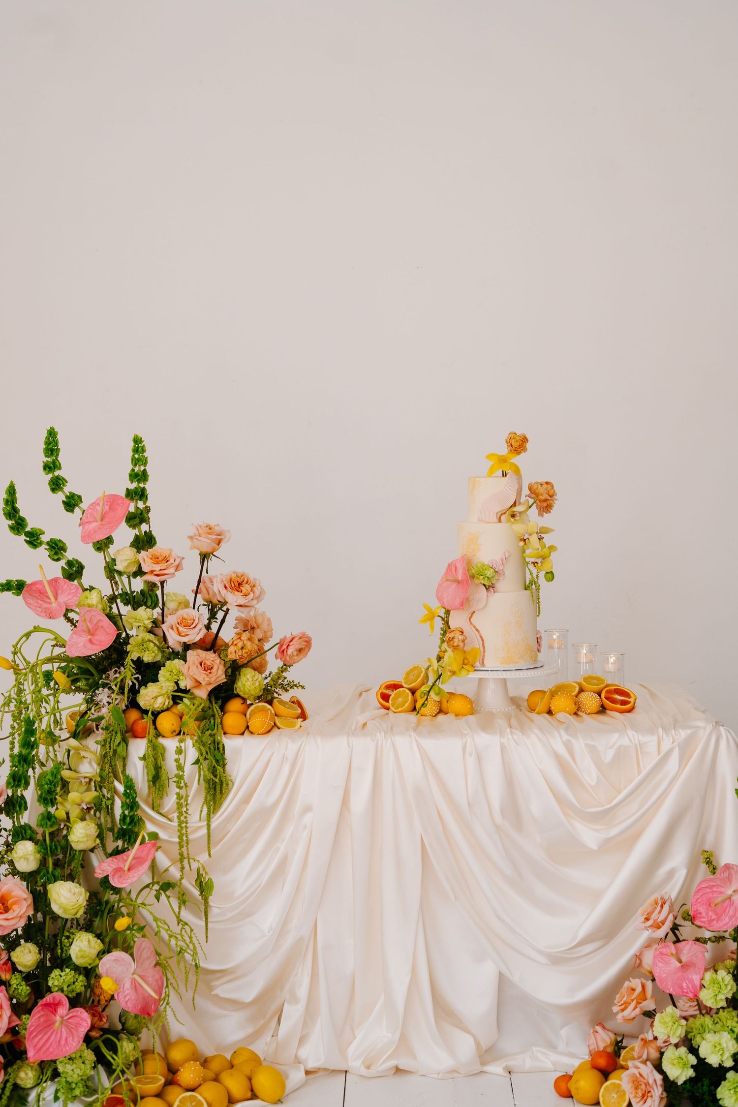 Elegant wedding table display with white satin tablecloth, pink roses, and fresh citrus fruits.