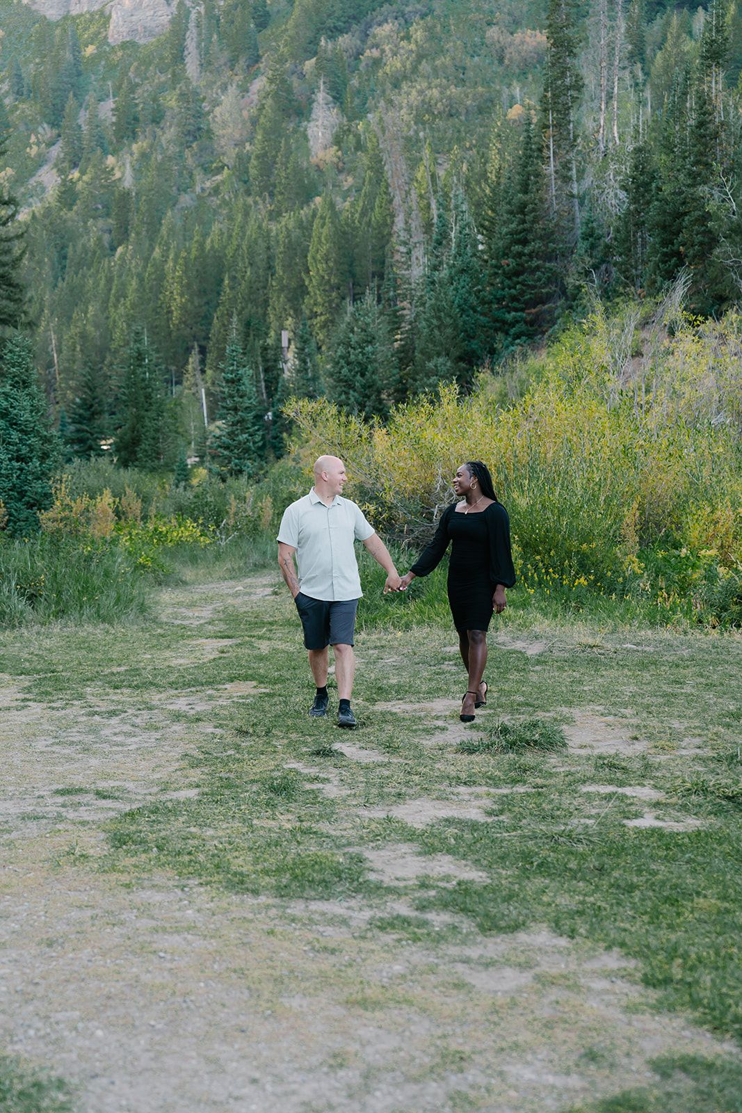 Couple walking hand in hand through a scenic mountain meadow.