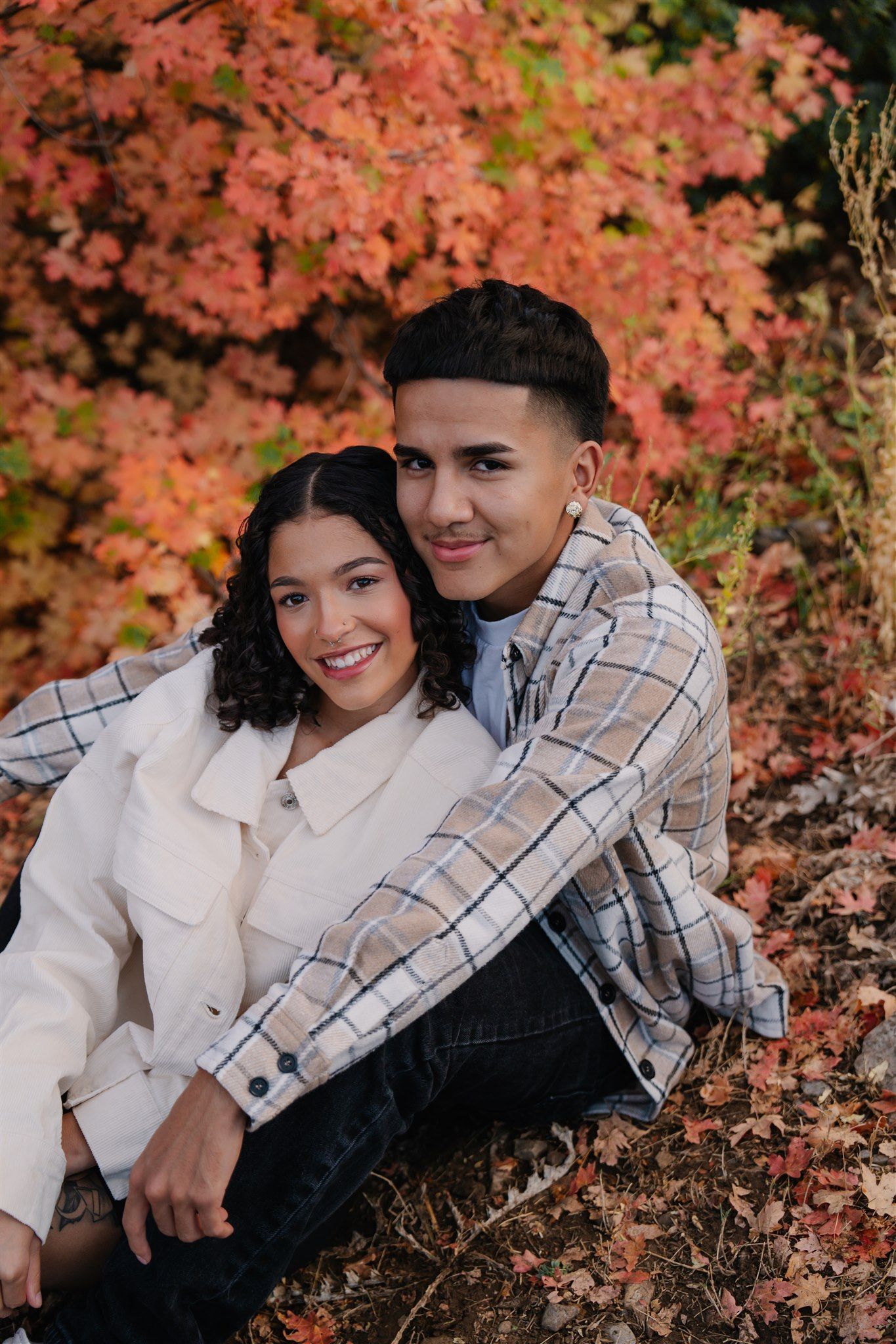 A couple poses together against vibrant autumn foliage with pink and orange leaves.
