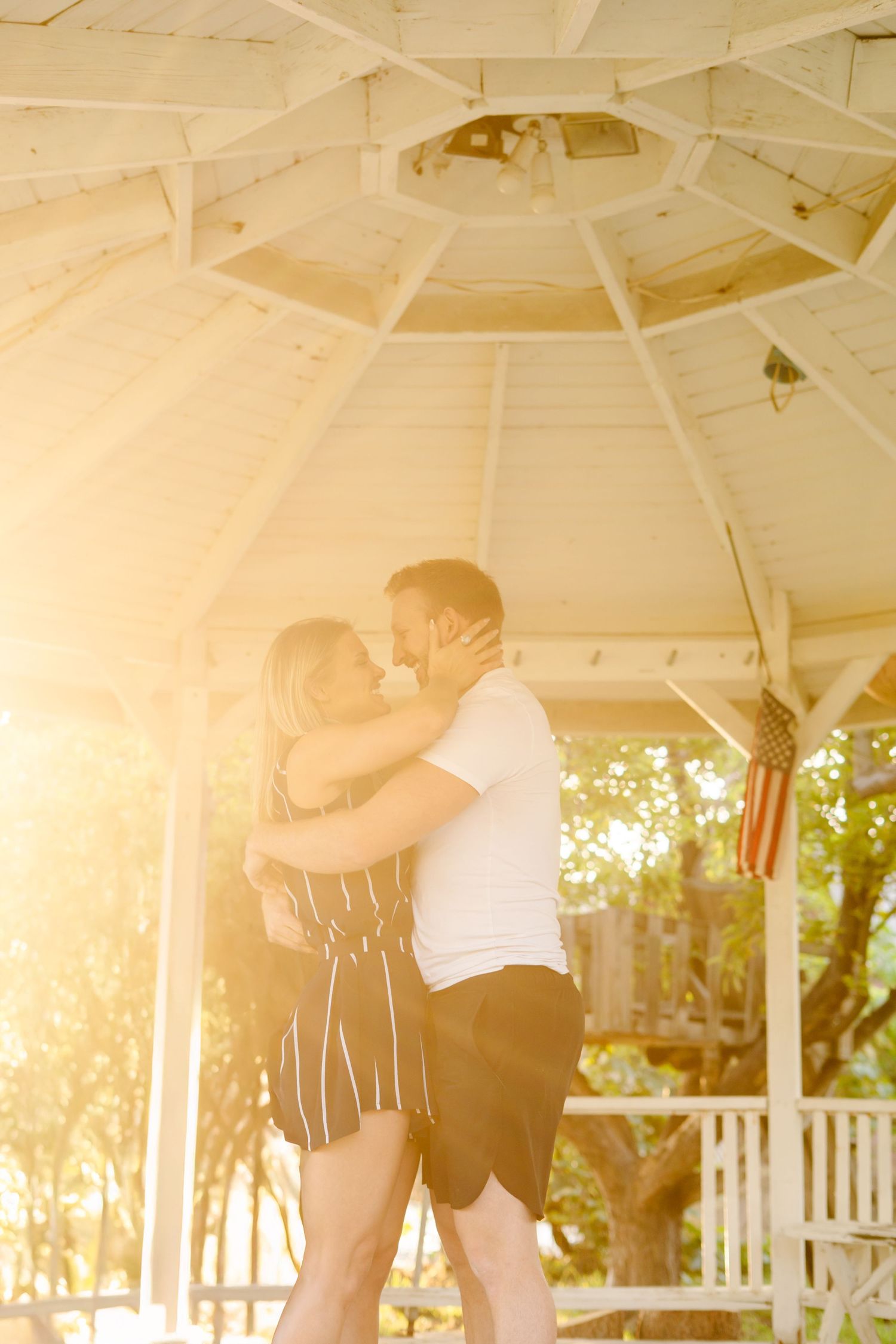 A tender moment shared under a white gazebo ceiling during golden hour.