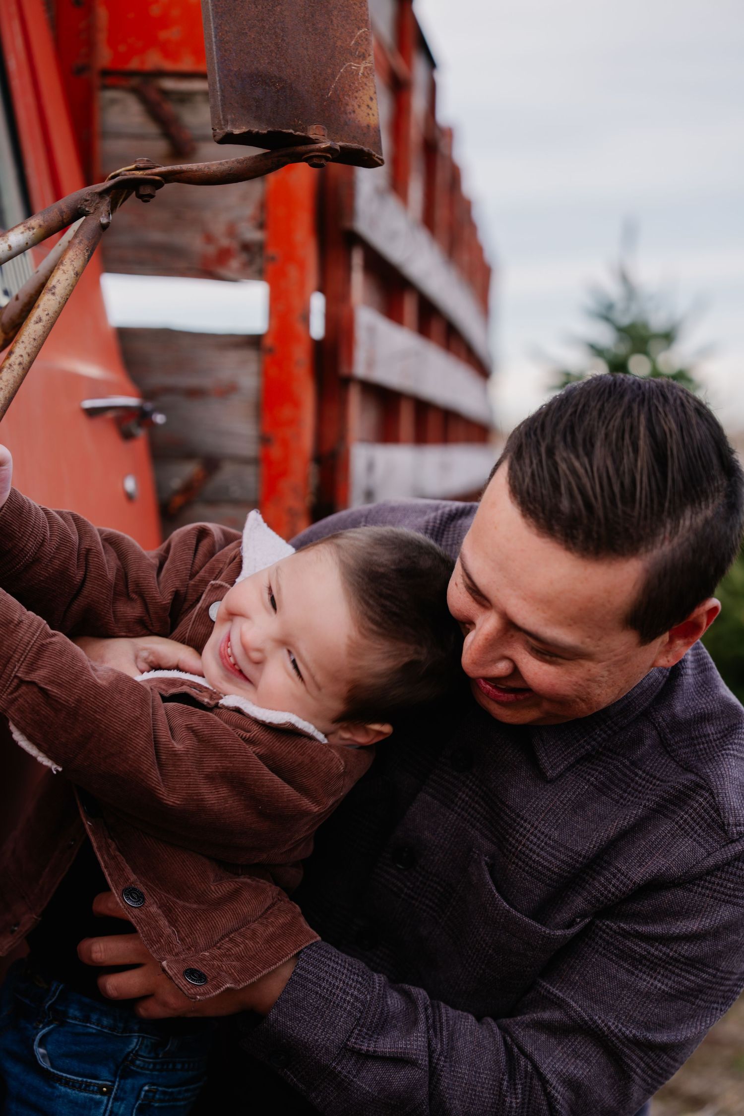 A father lovingly holds his smiling toddler near a rustic red barn, sharing a joyful outdoor moment.