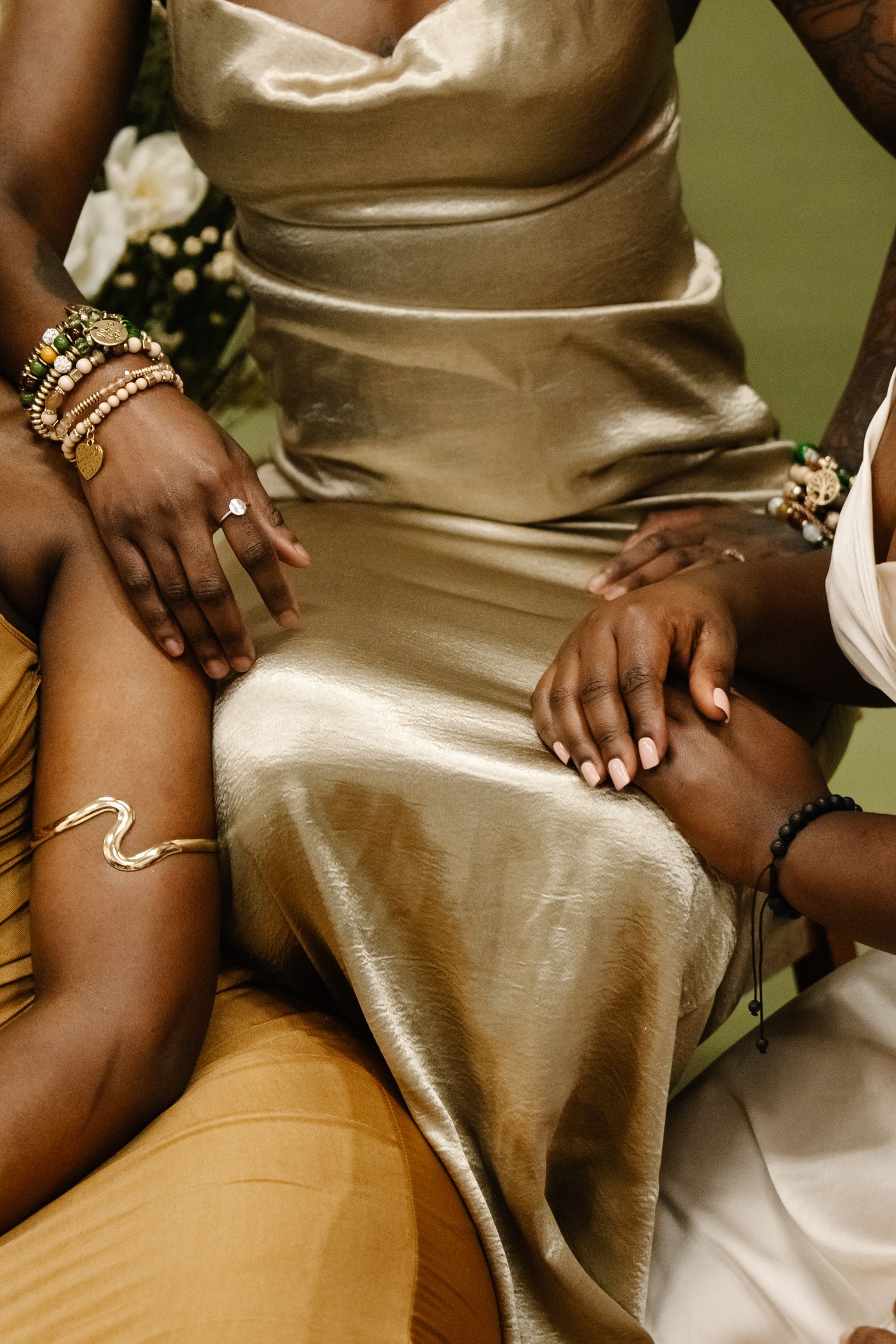 Detail shot of gold silk dresses and jewelry against neutral background.