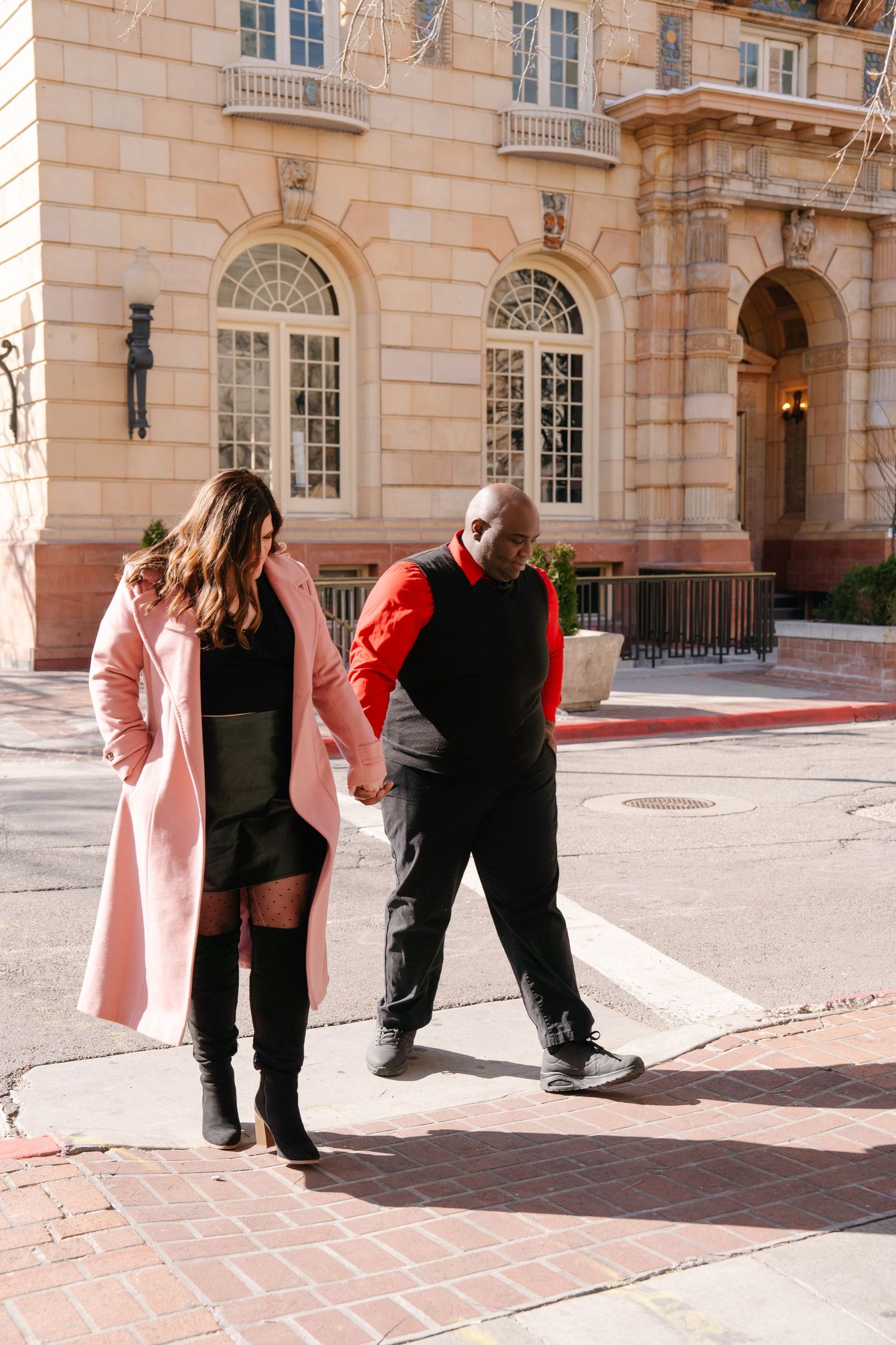 A couple shares a tender moment outside a grand stone building with arched windows.