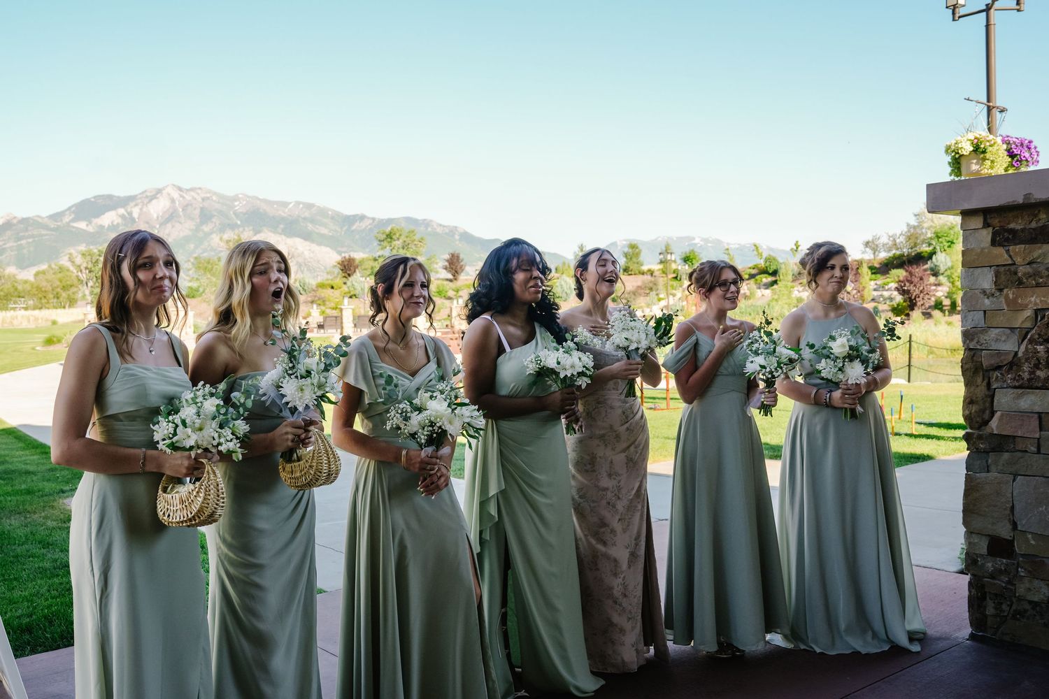 Wedding party in sage green dresses lined up outdoors.