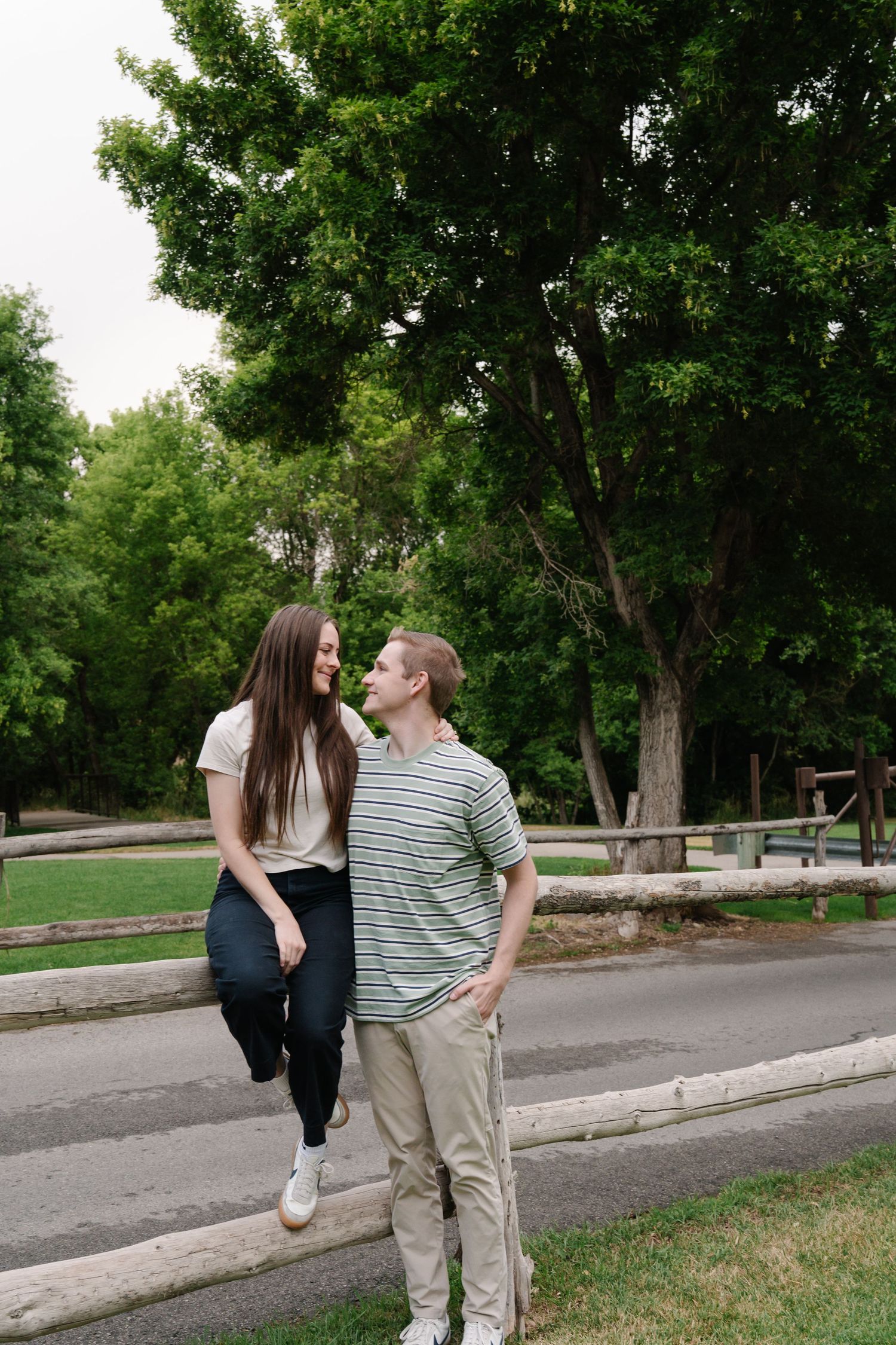 A couple shares a playful interaction on a tree-lined street.