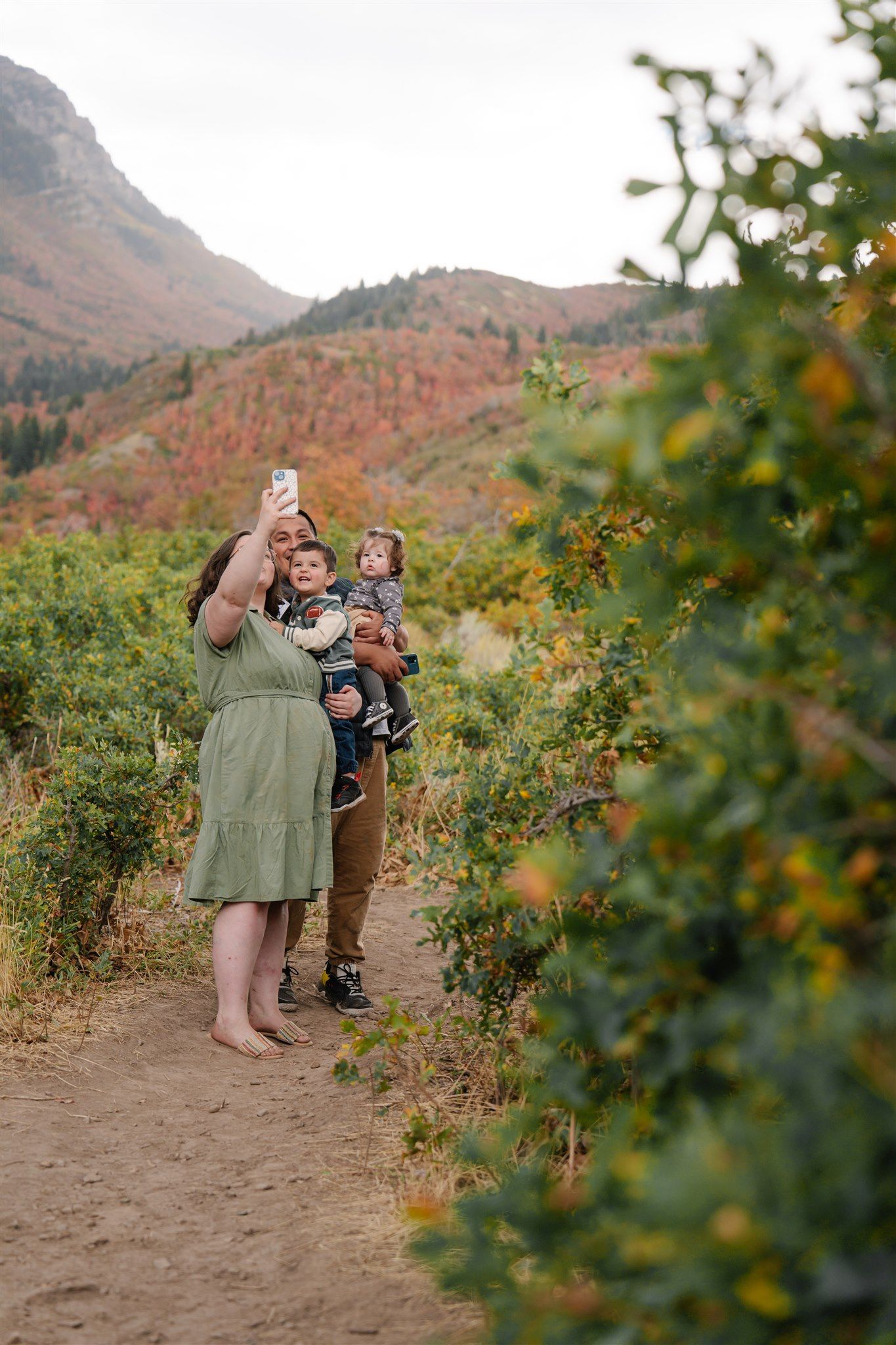 Family taking photos together on dirt path with mountain scenery and desert brush.