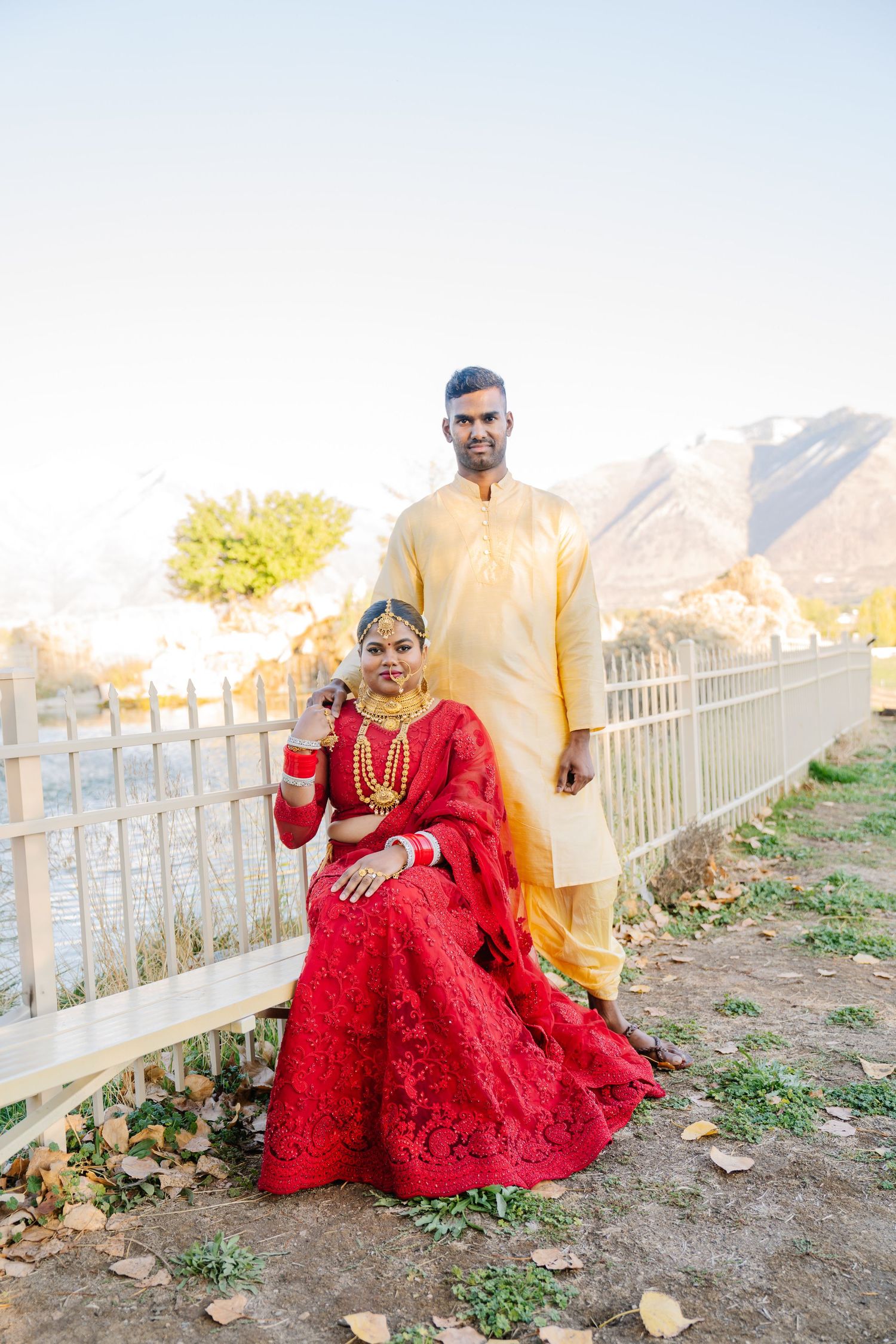 A couple in traditional South Asian attire posing against a mountain landscape backdrop.