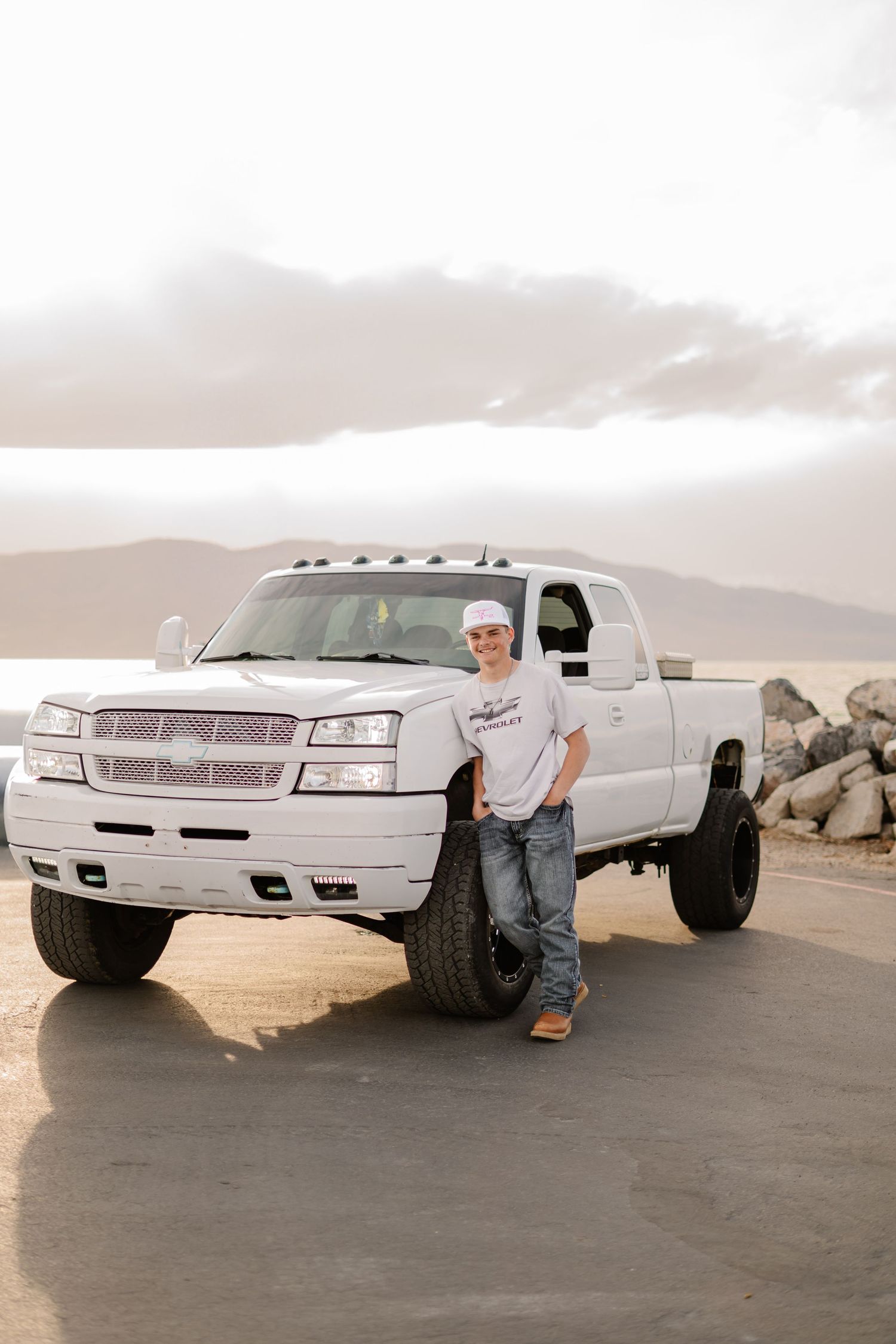 White customized pickup truck displayed against desert mountain landscape.