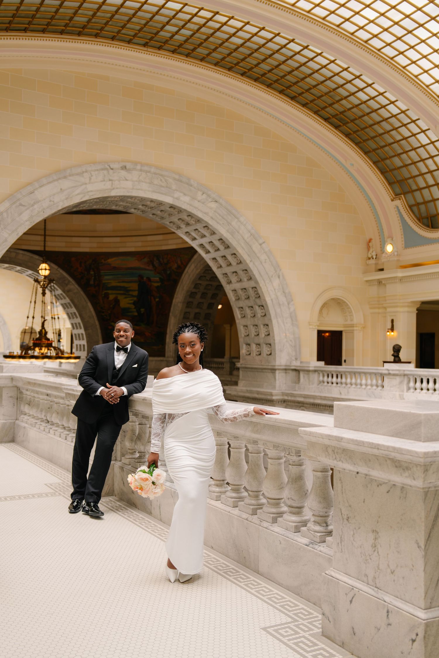 Elegant Black couple in wedding attire pose inside a grand marble hall with arched ceilings and ornate details.