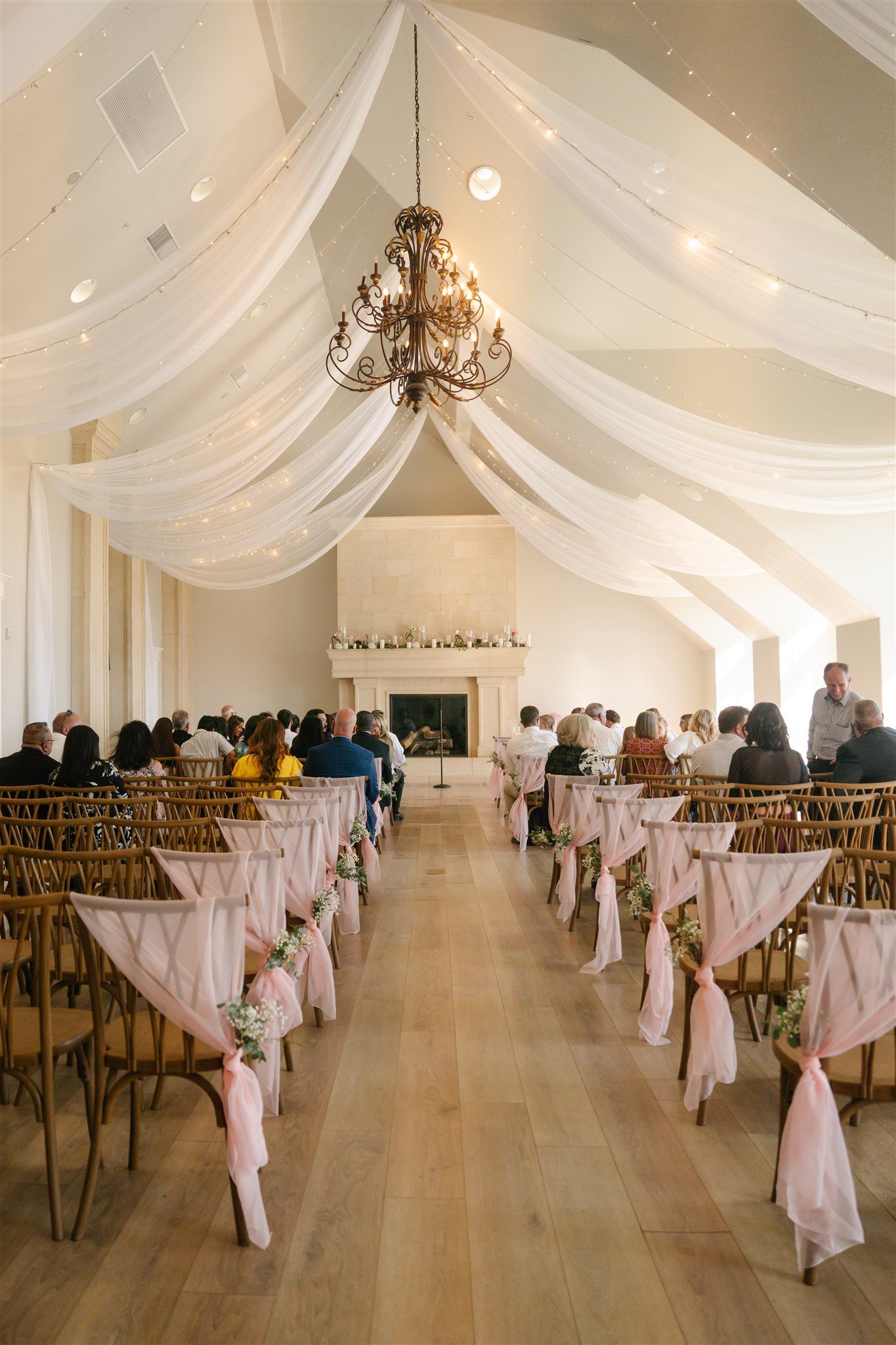 Elegant wedding reception hall decorated with white draping and chandeliers.