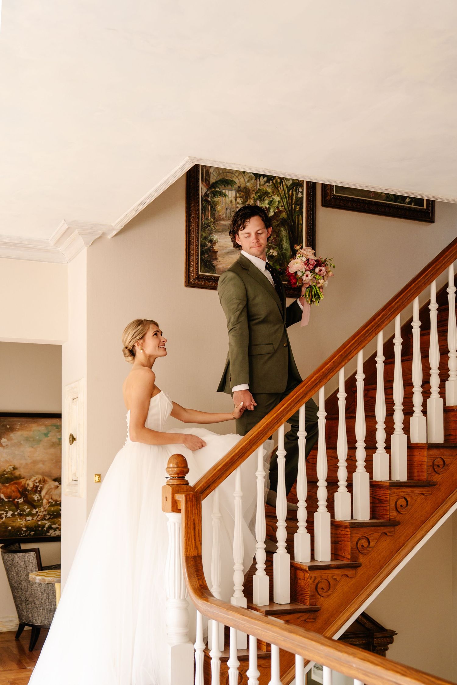 Wedding day first look moment captured on an elegant wooden staircase indoors.