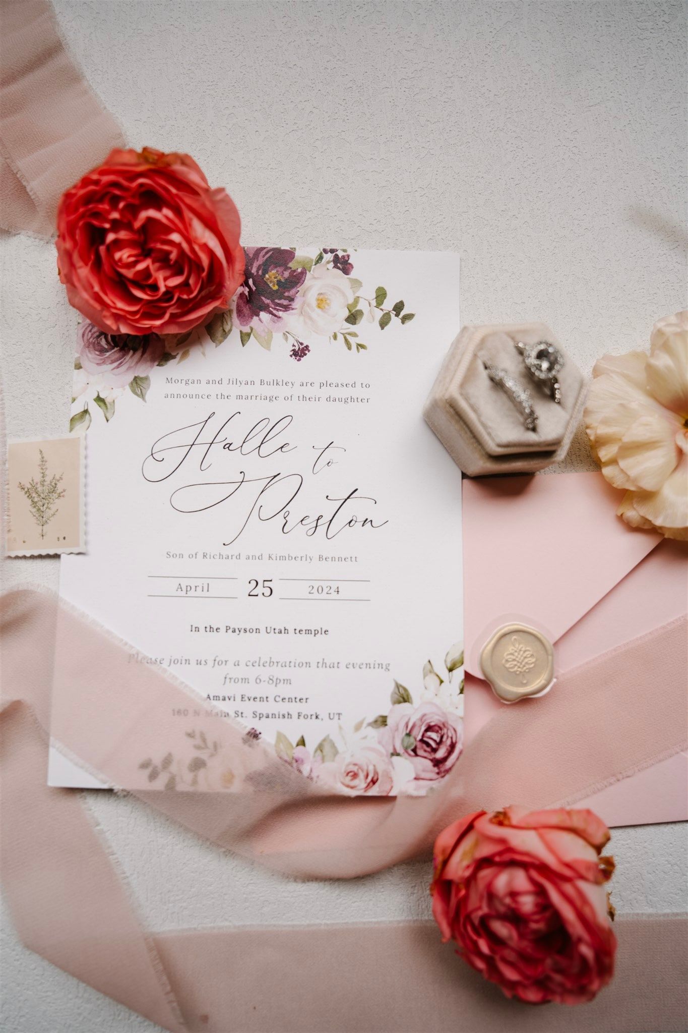 Romantic wedding stationery with floral details and wax seals on pink background.