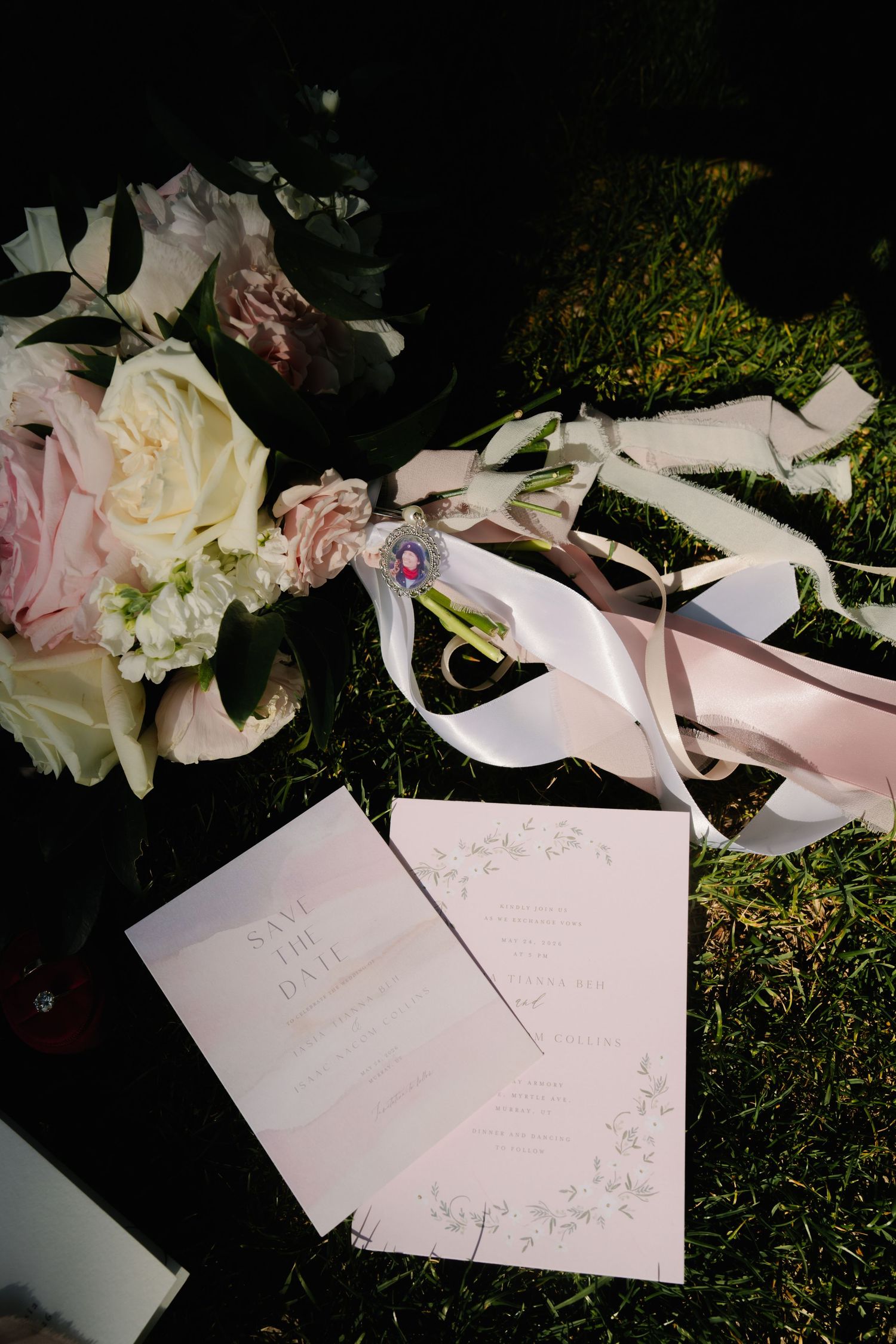 Elegant wedding stationery with save the date cards beside a pink and white floral bouquet with ribbon on green grass.