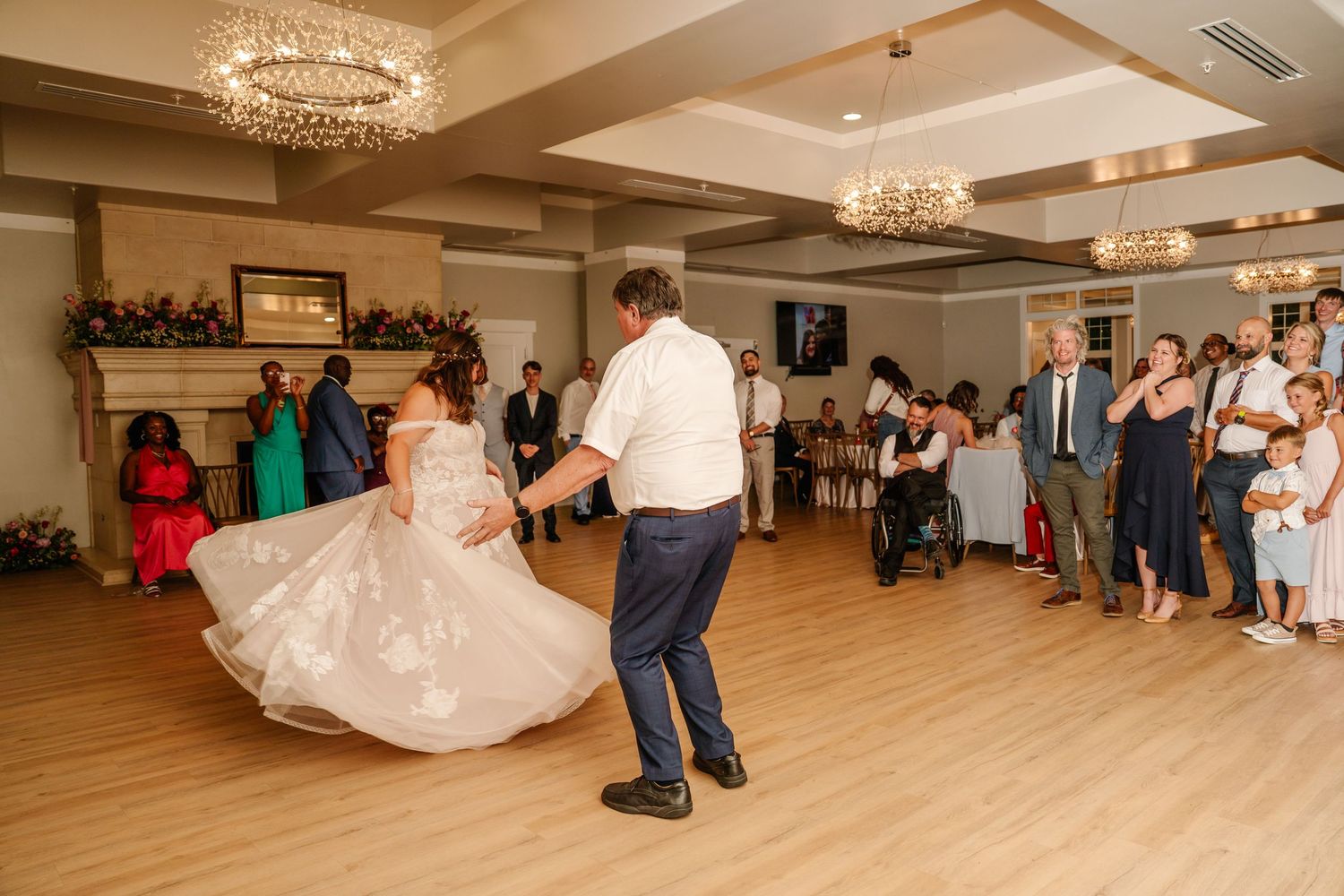 Couple dancing together on wooden floor as wedding guests watch from the sidelines.