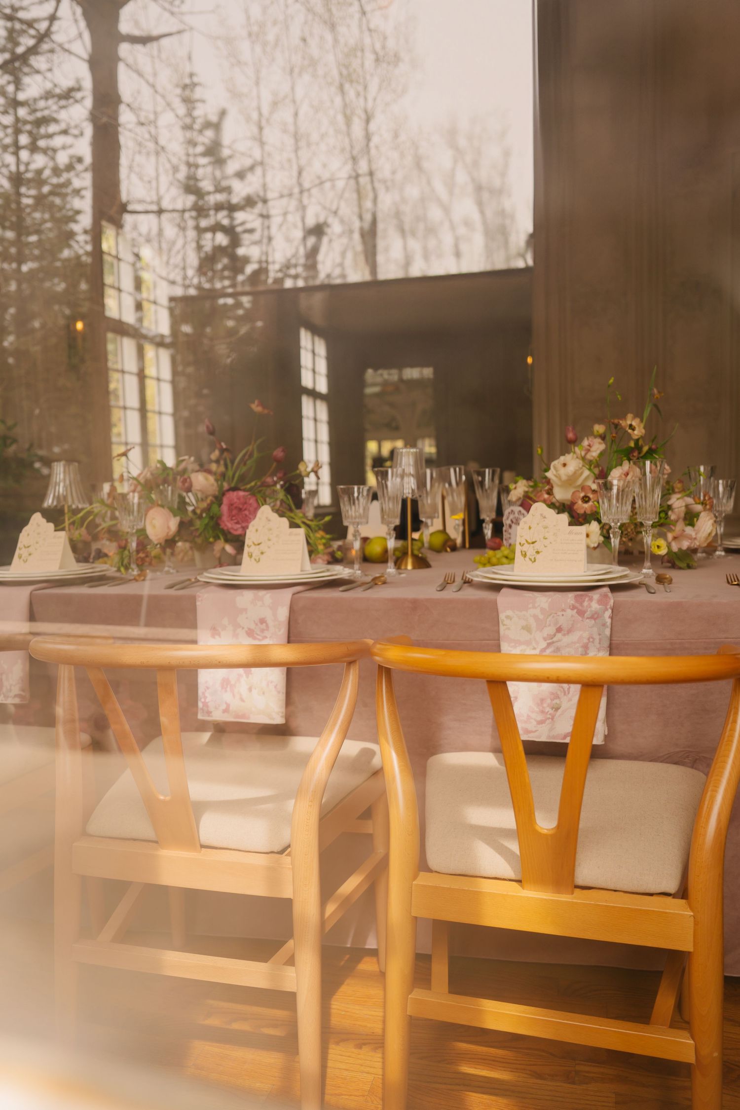 Elegant wooden chairs and table settings arranged in a sunlit room with forest views through large windows.