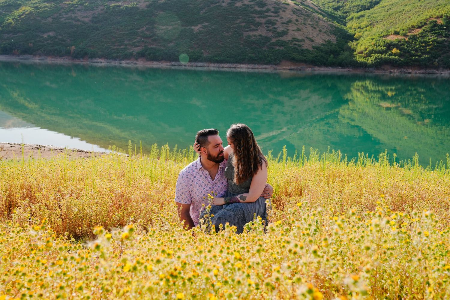 Couple enjoying romantic moment in wildflower field beside emerald mountain lake.