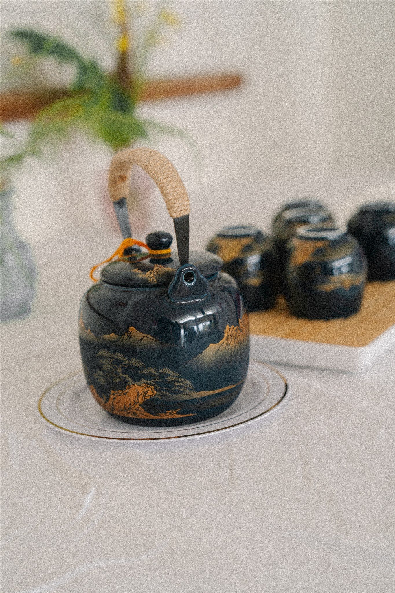 A decorative black Asian teapot with gold details displayed alongside other teaware on a white surface.