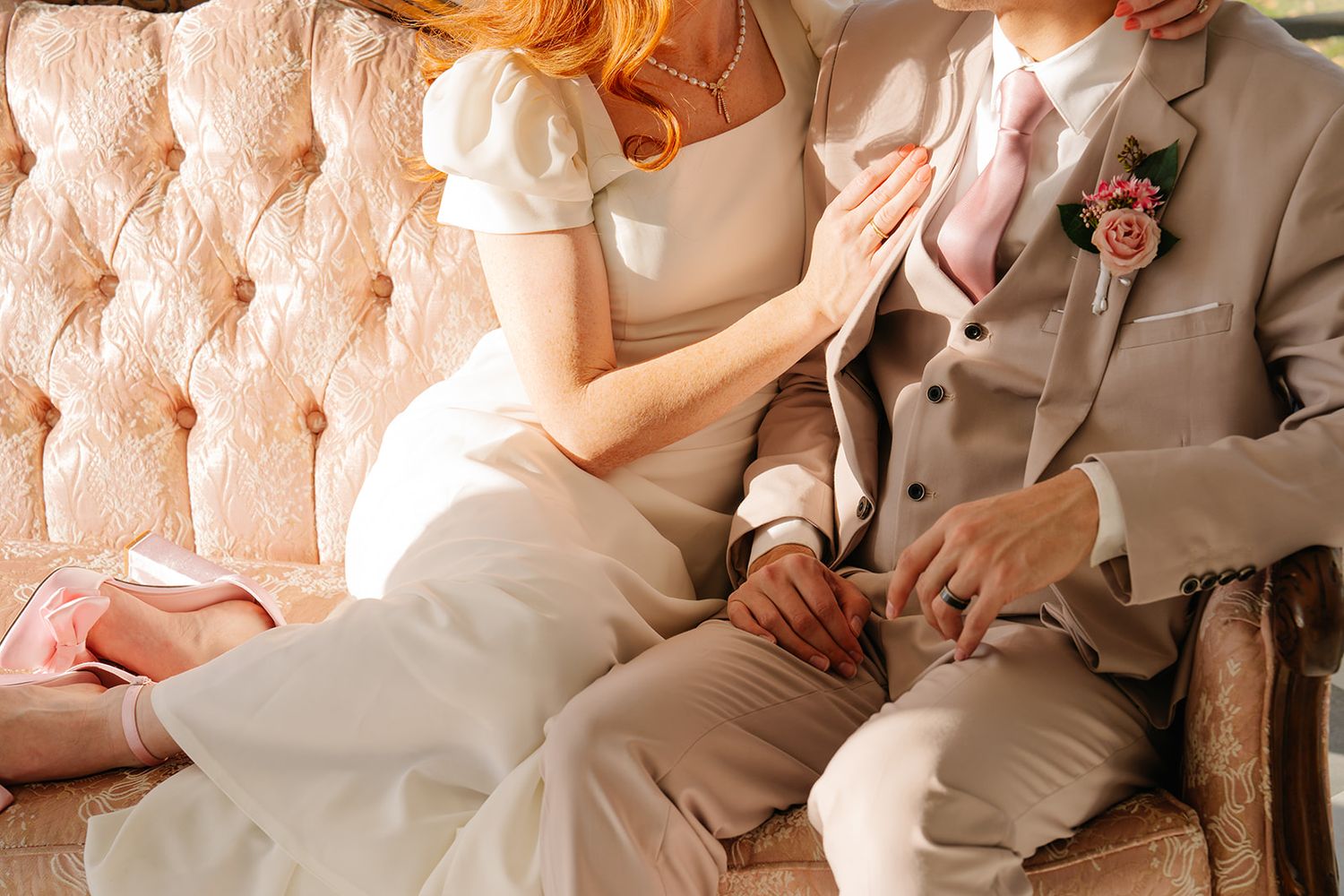 A couple sits close together on a tufted vintage couch in formal wedding attire.