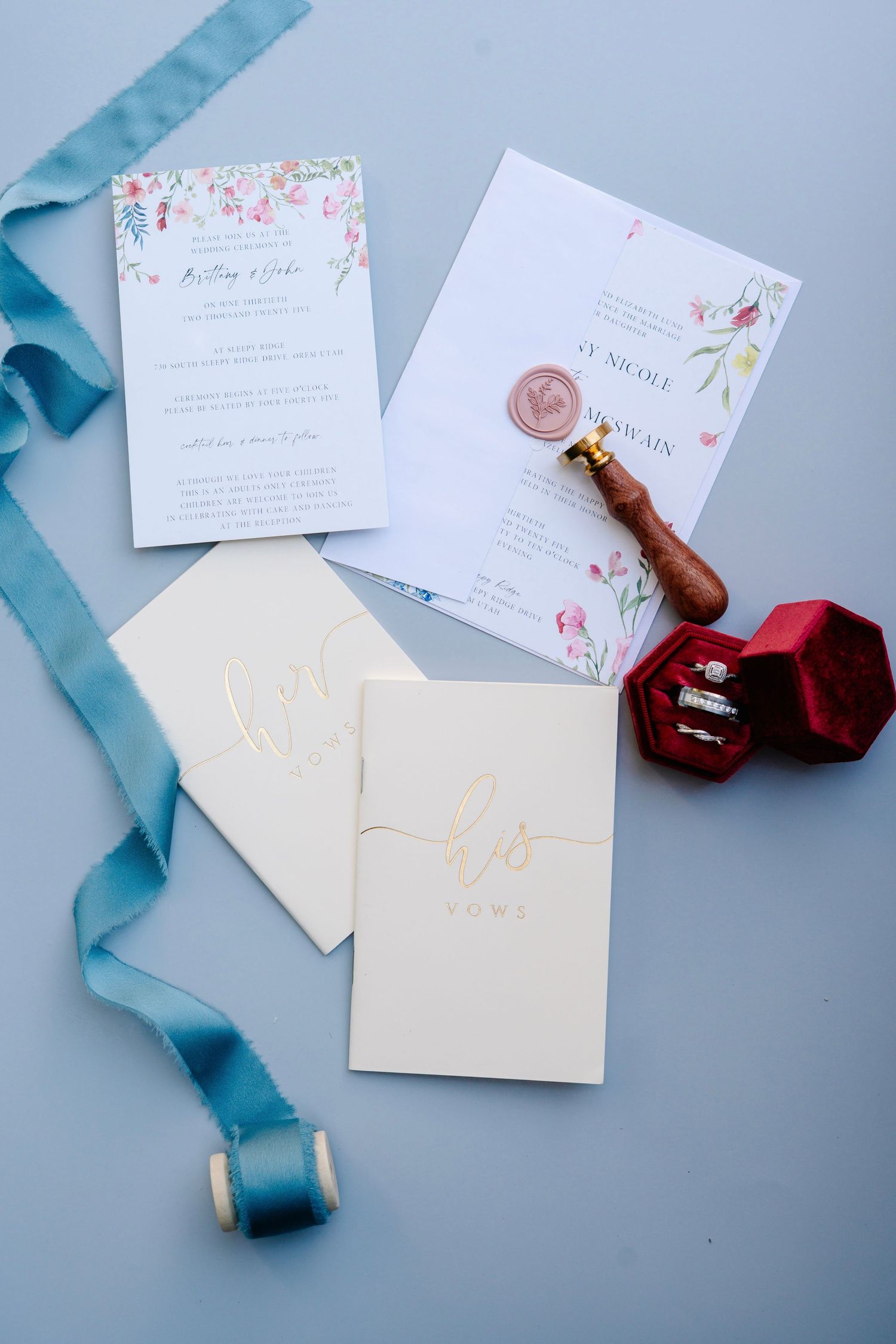 Wedding stationery with blue ribbon and wax seal laid out on pale blue surface.