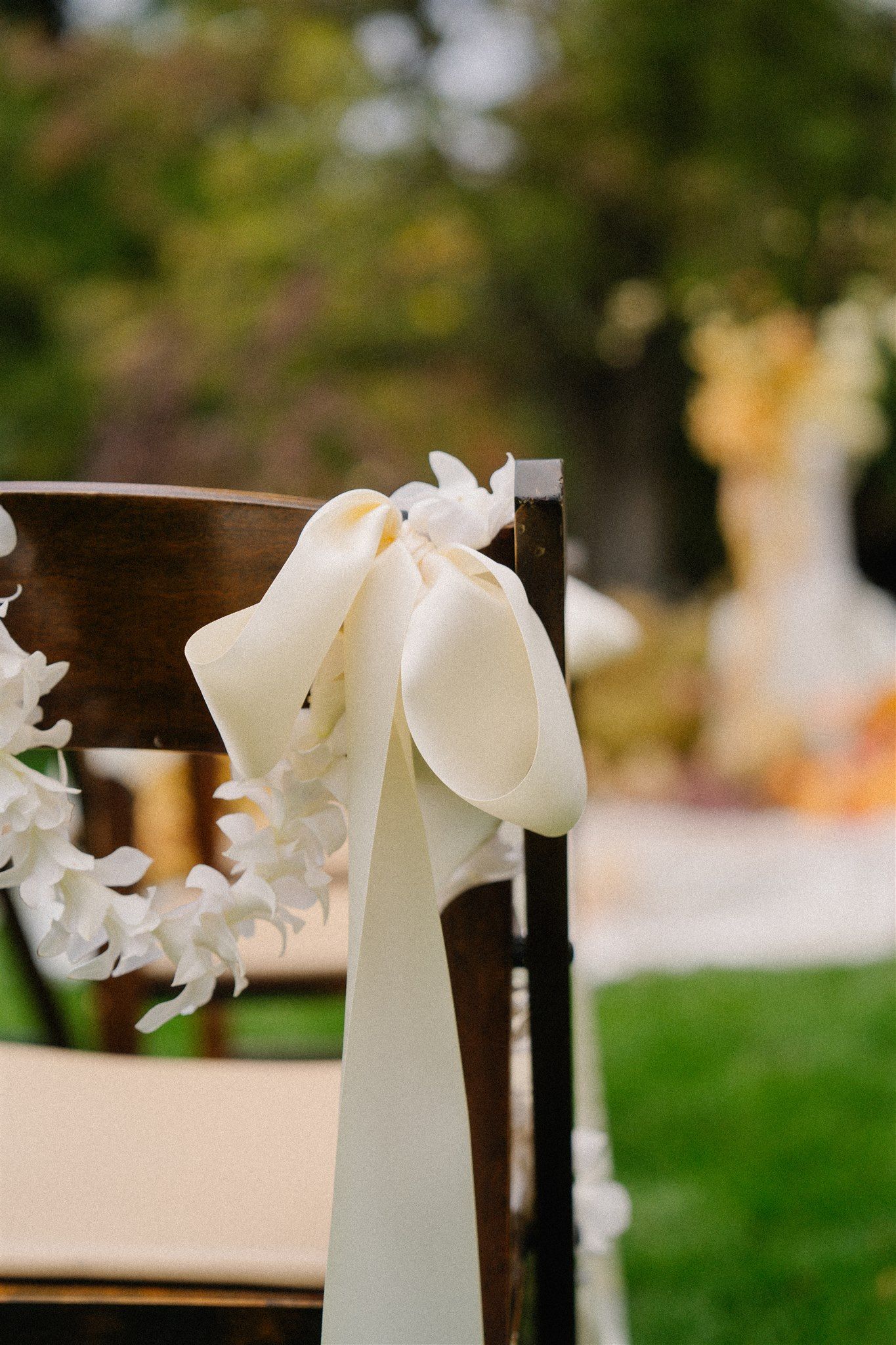 White decorative bows adorning dark wooden chairs for a wedding ceremony.