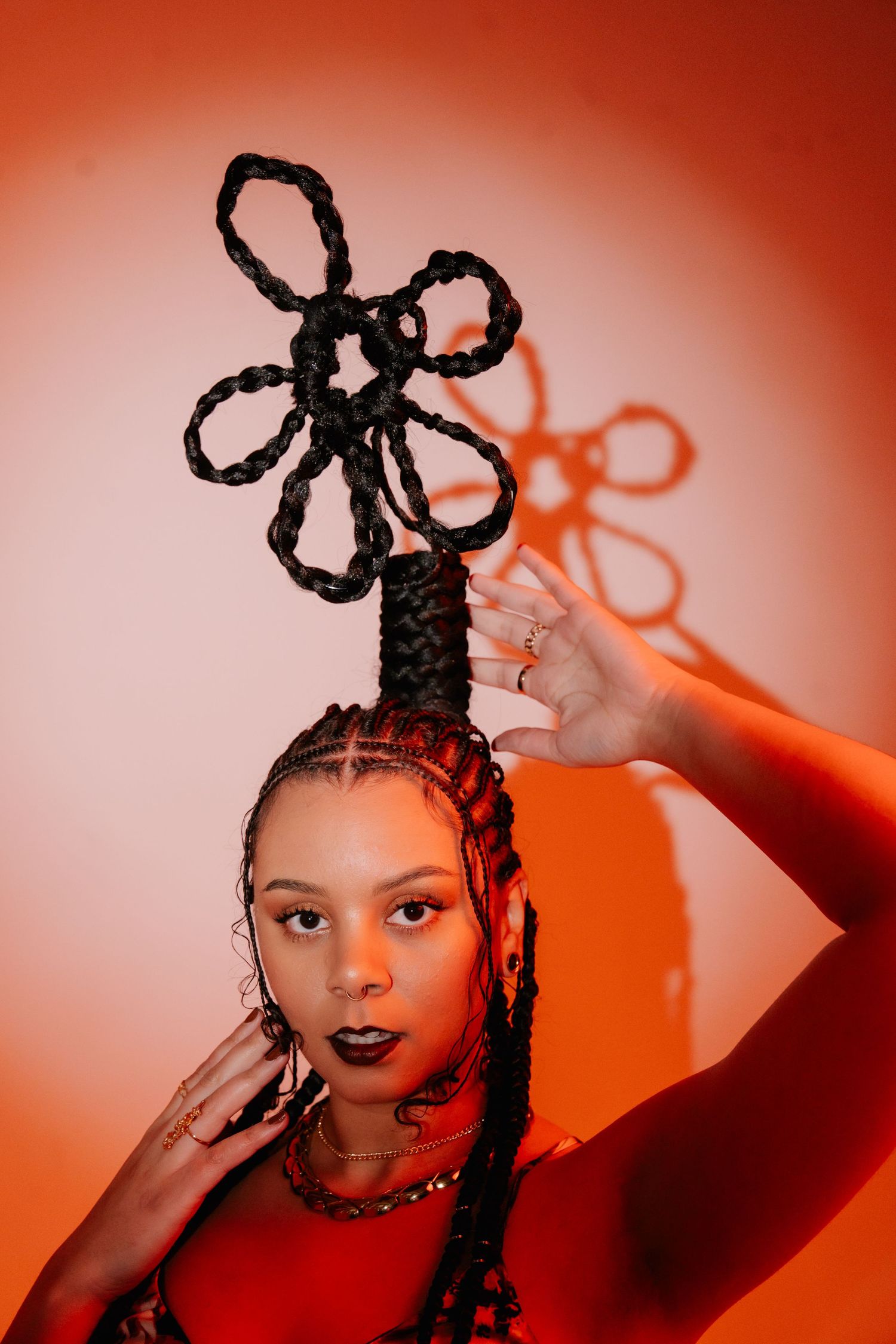 Artistic portraits with unique braided hairstyles against a vibrant orange background.