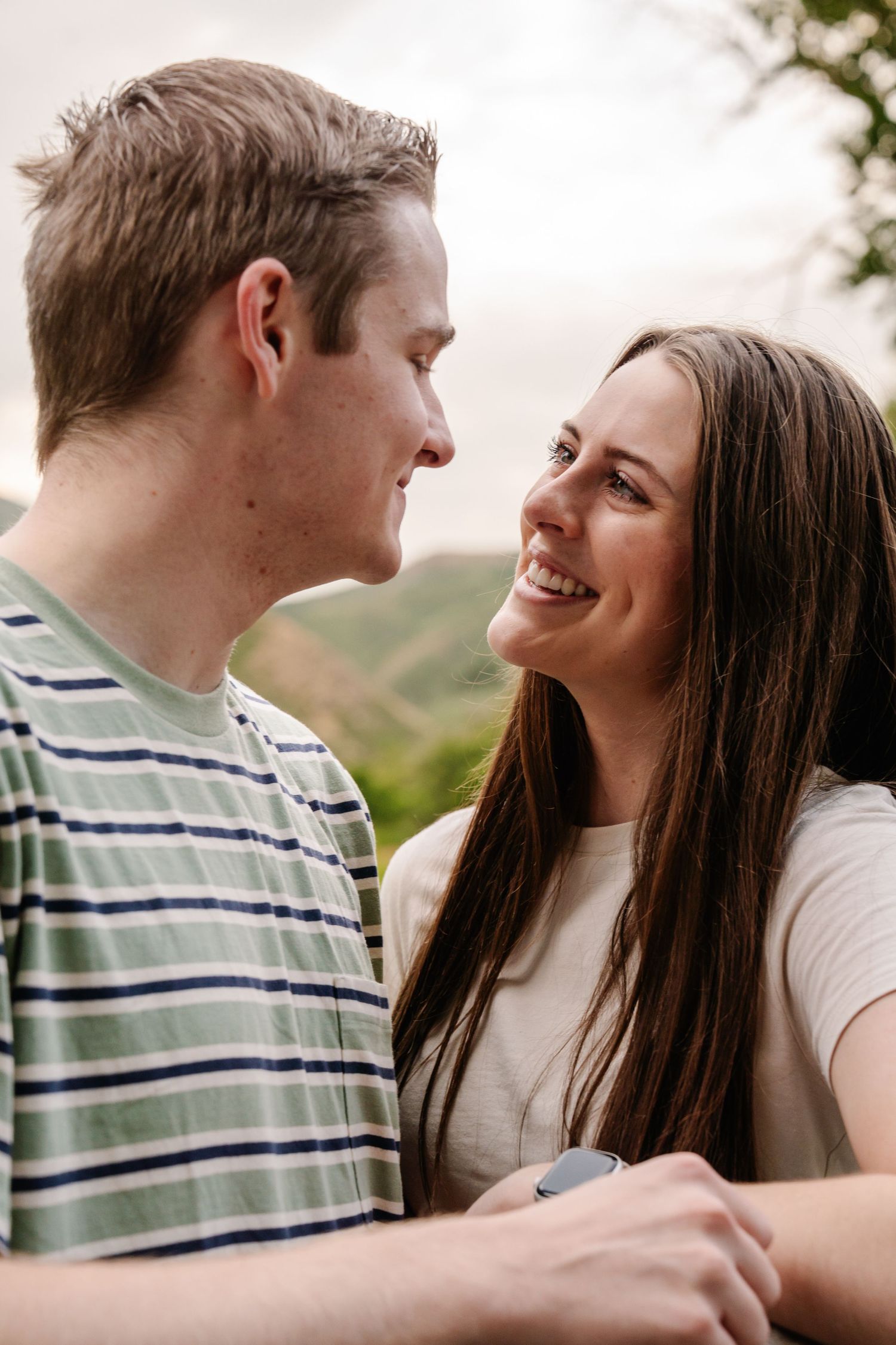 Two people share affectionate glances against a natural backdrop.