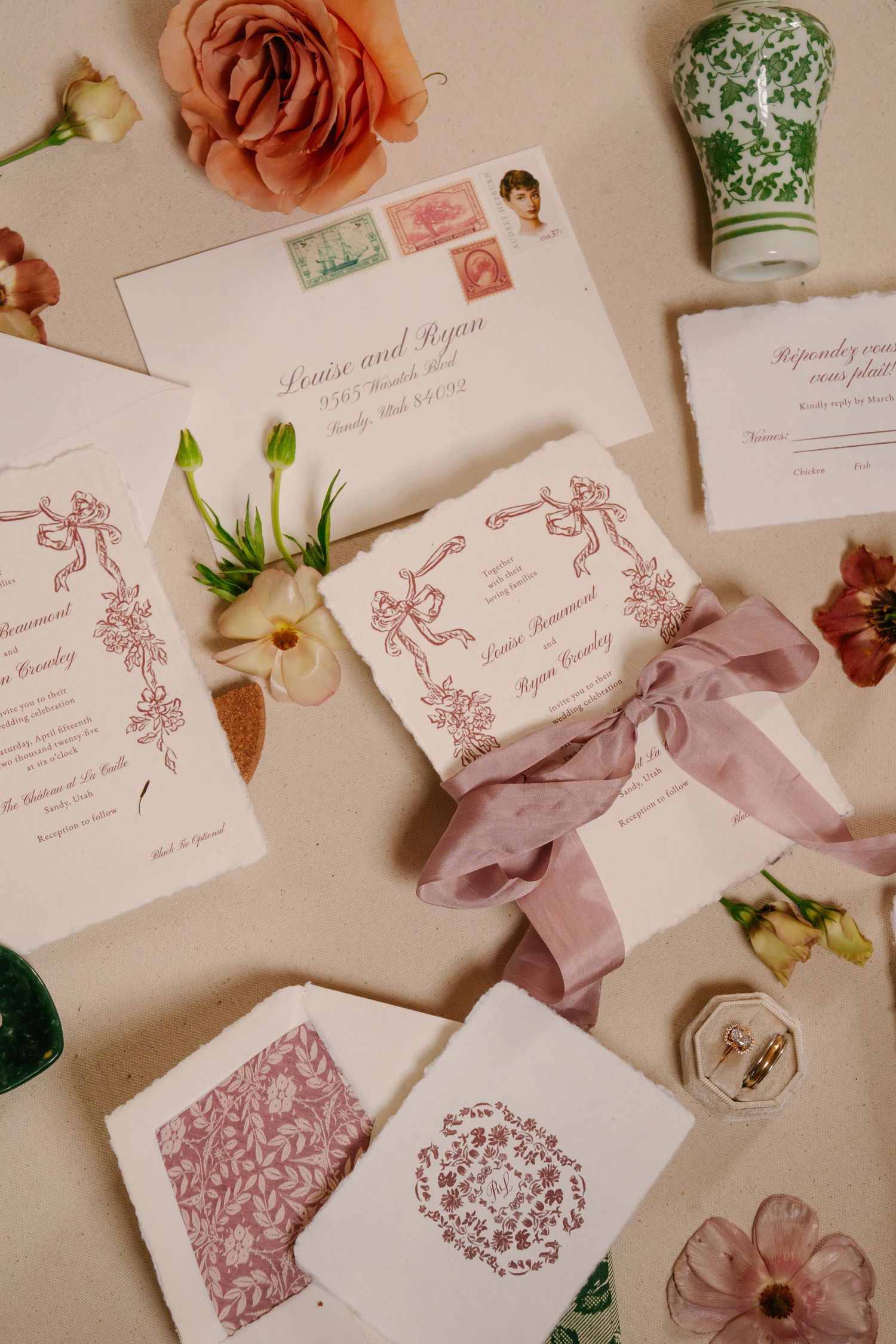 Elegant wedding invitations with pink floral designs and silk ribbons arranged on a light surface.