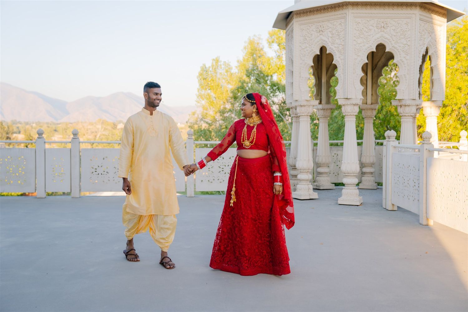 Elegant couple walking through a grand white colonnade with mountain views.