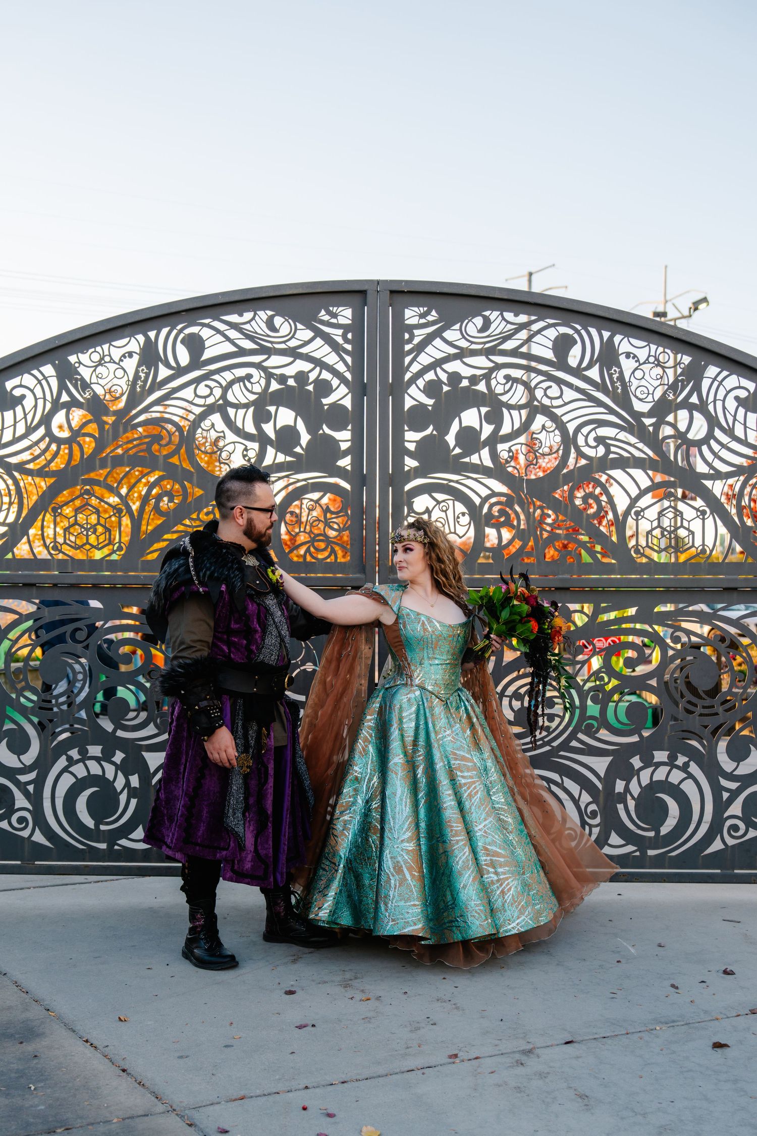Ornate wrought iron gate serves as backdrop for formal event with people in elegant gowns.