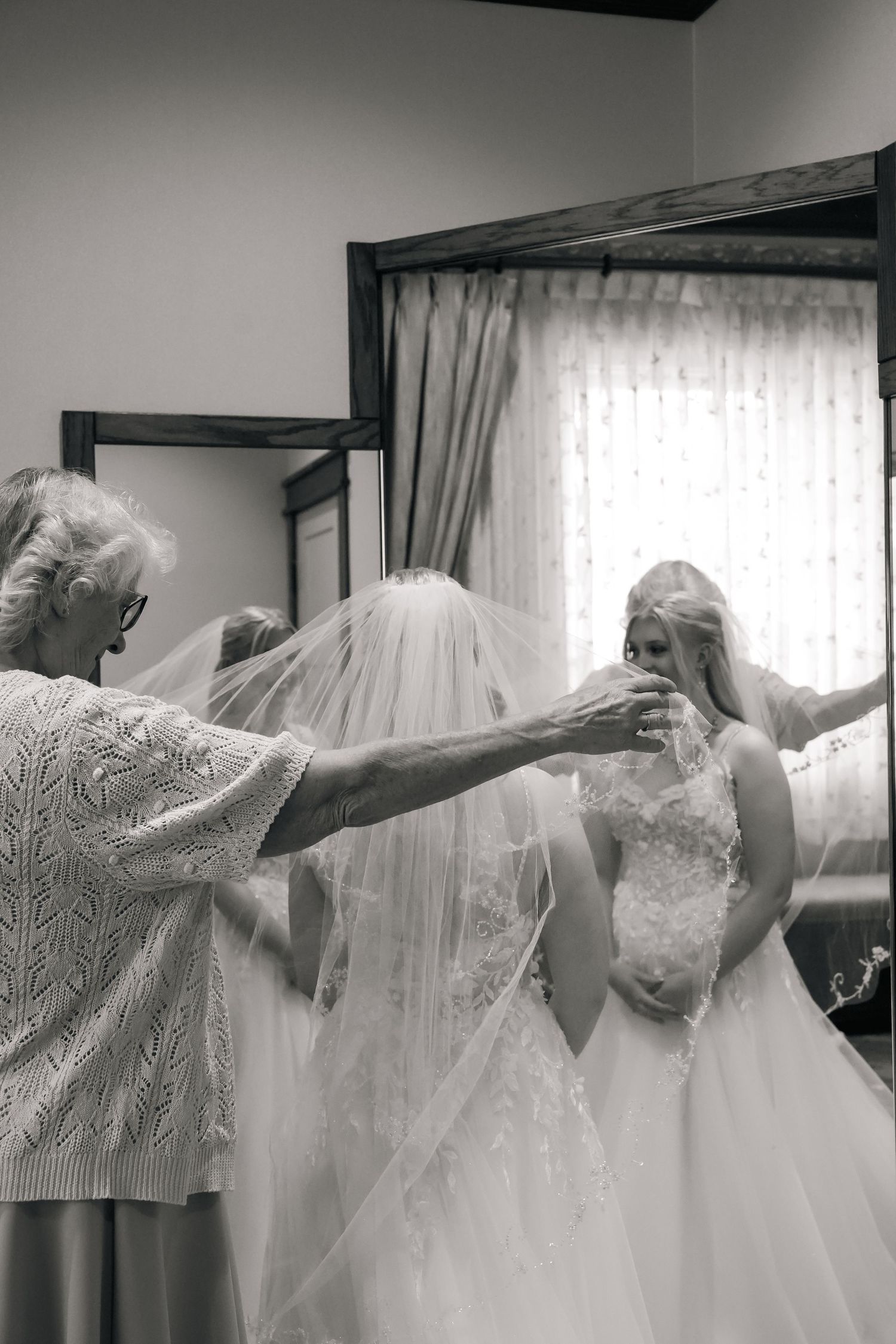 Bride and bridesmaids in white dresses pose playfully with outstretched arms in a getting ready room.