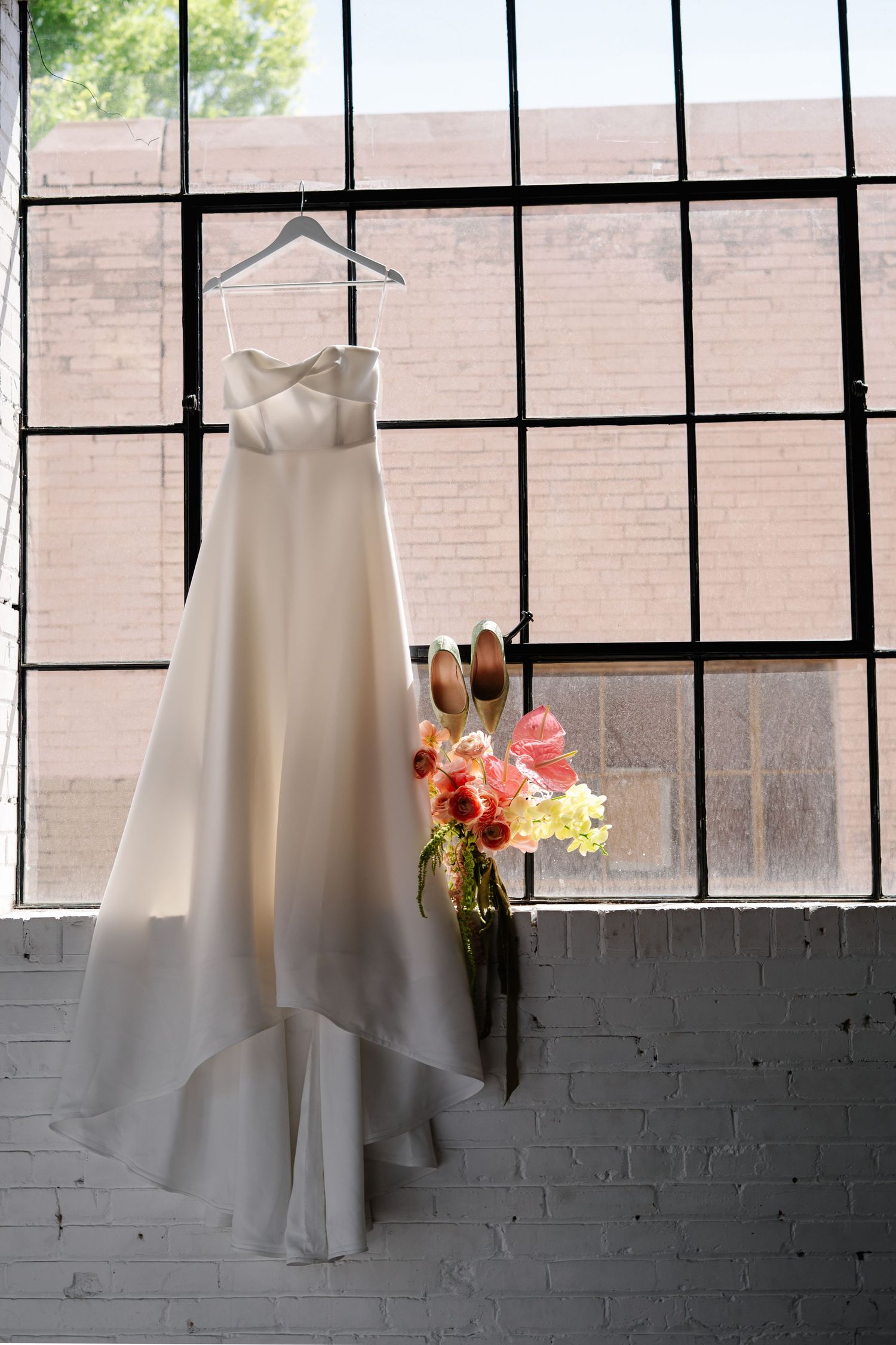 White wedding dresses hanging in a row against industrial windows with natural light.