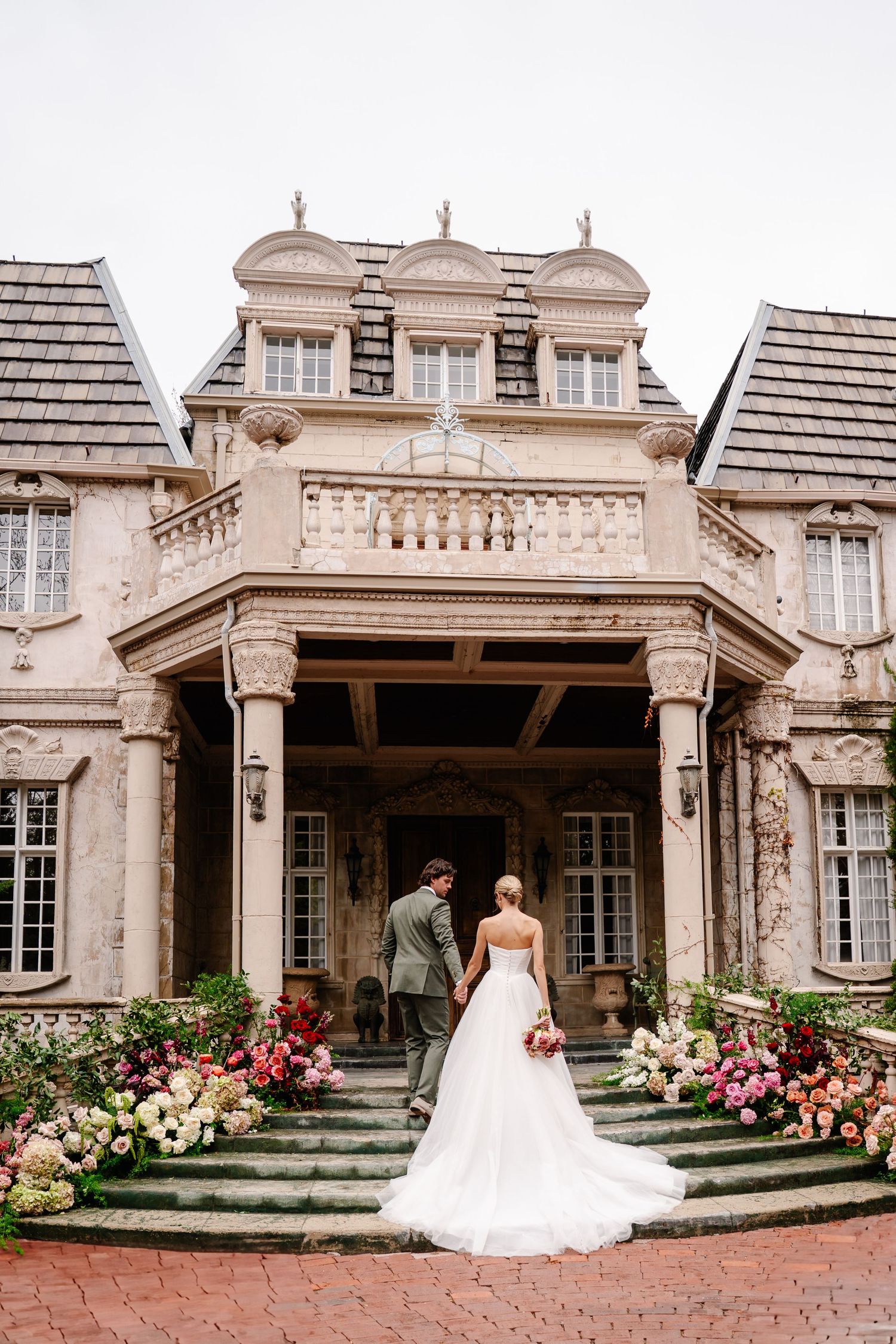 Classic mansion exterior with white columns and blooming flower gardens creates an elegant bridal portrait backdrop.