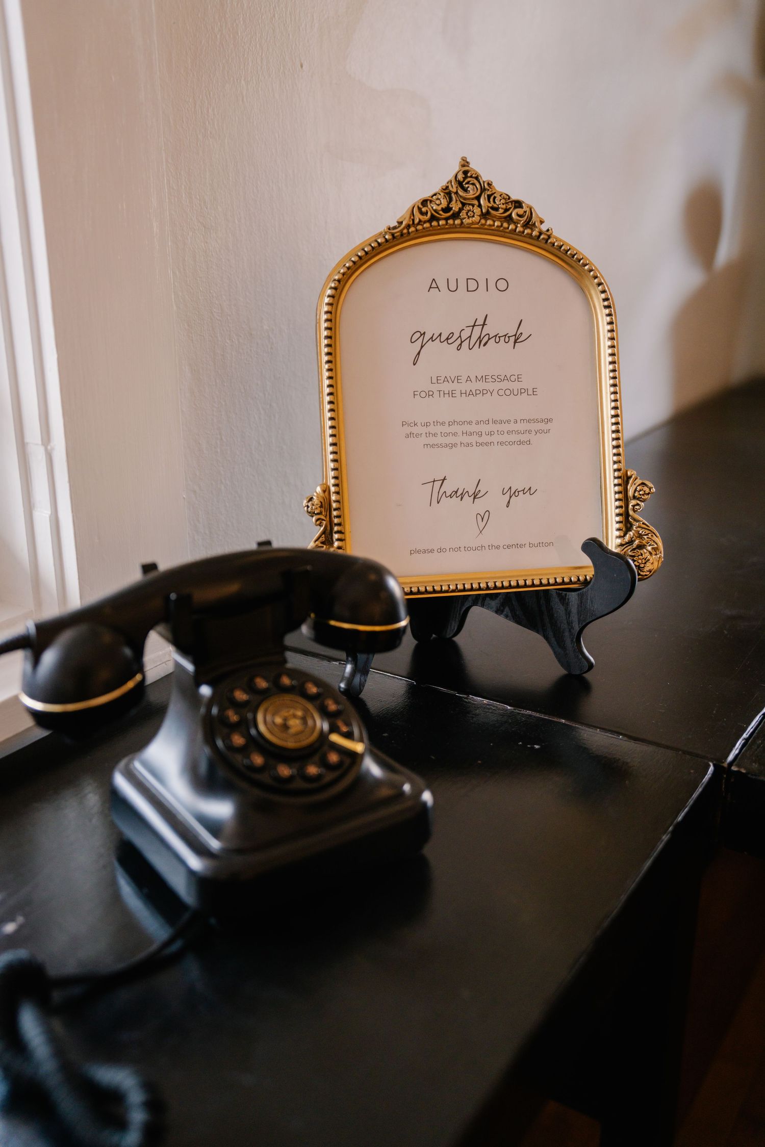 Vintage black rotary phone beside a gold framed audio guestbook sign at a wedding reception.