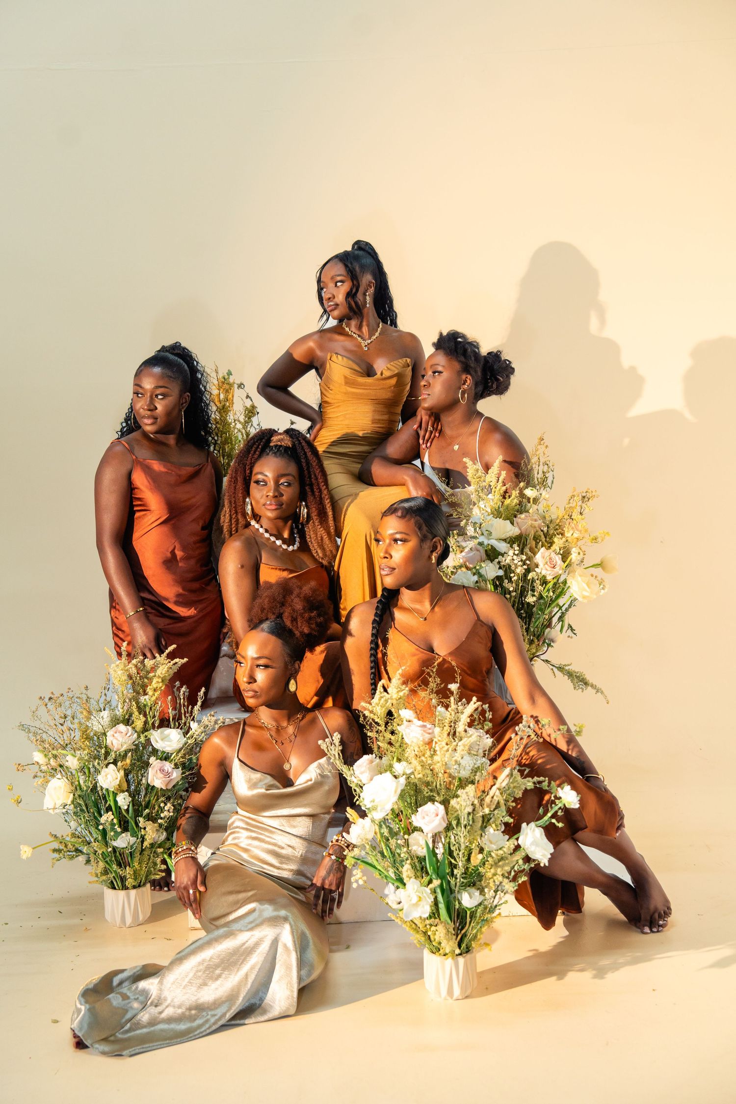 Models in earth-toned dresses arranged artistically with white floral arrangements.