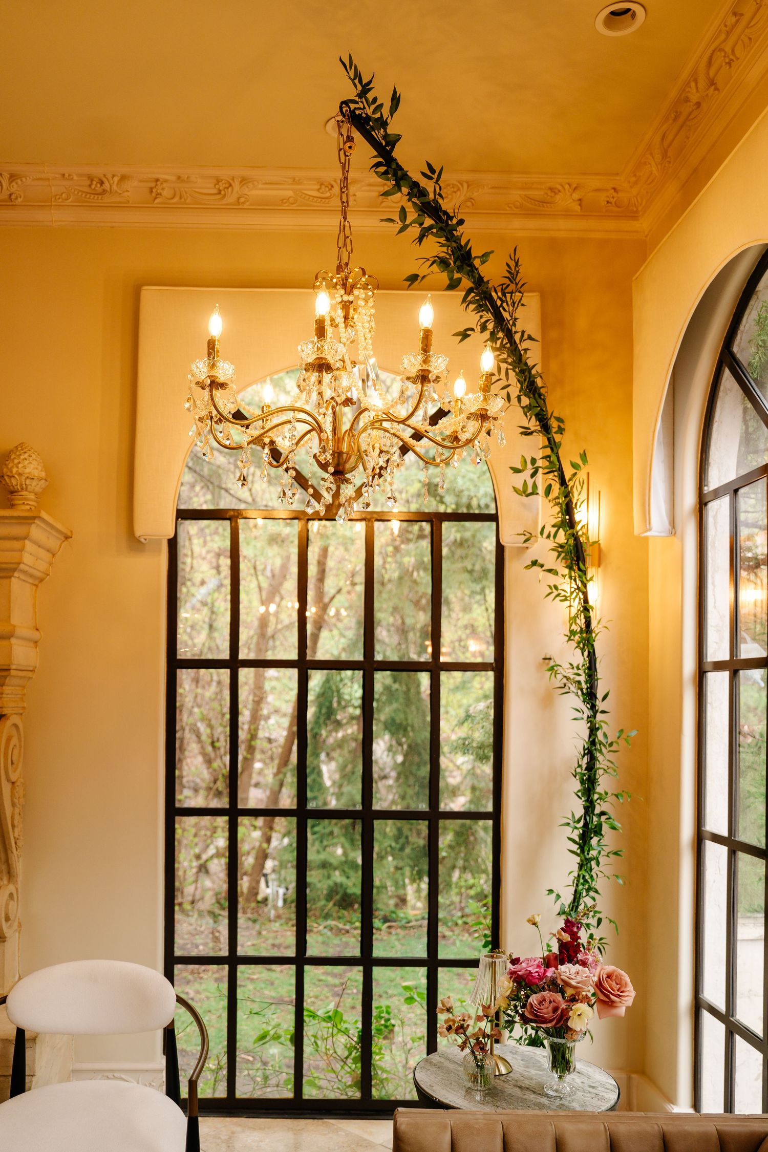 Elegant indoor venue space with crystal chandeliers and climbing vines framing arched windows.