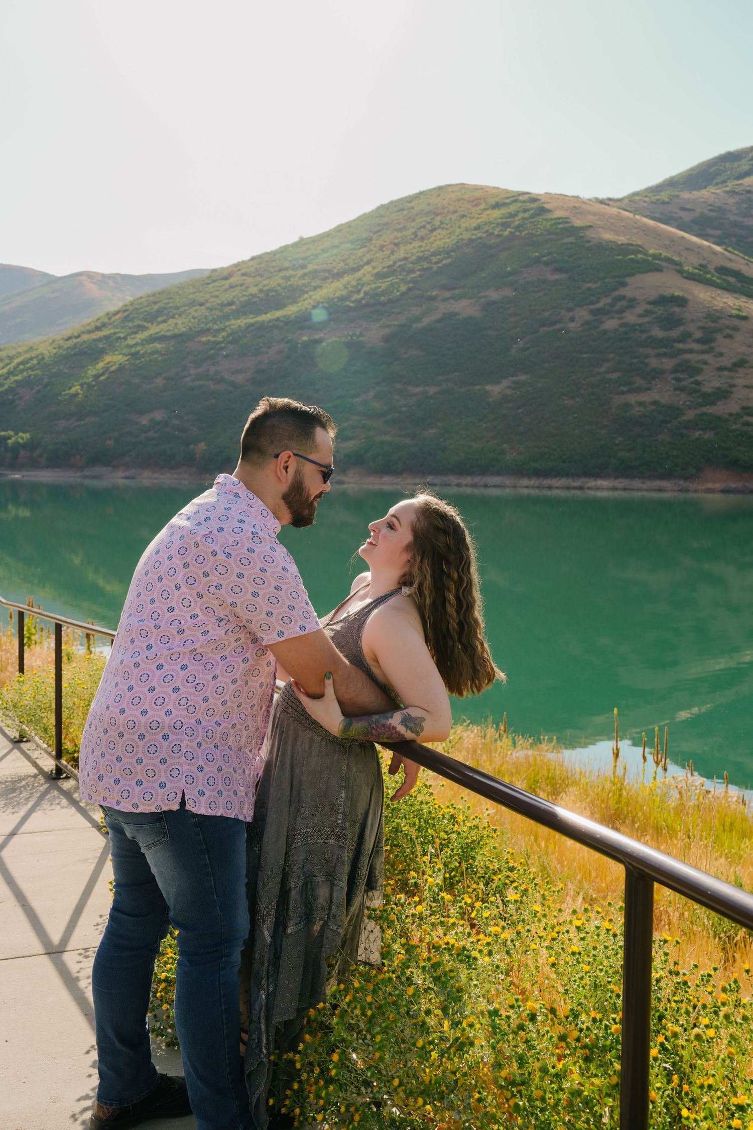 Couple sharing a laugh while leaning against railing overlooking mountain lake view.