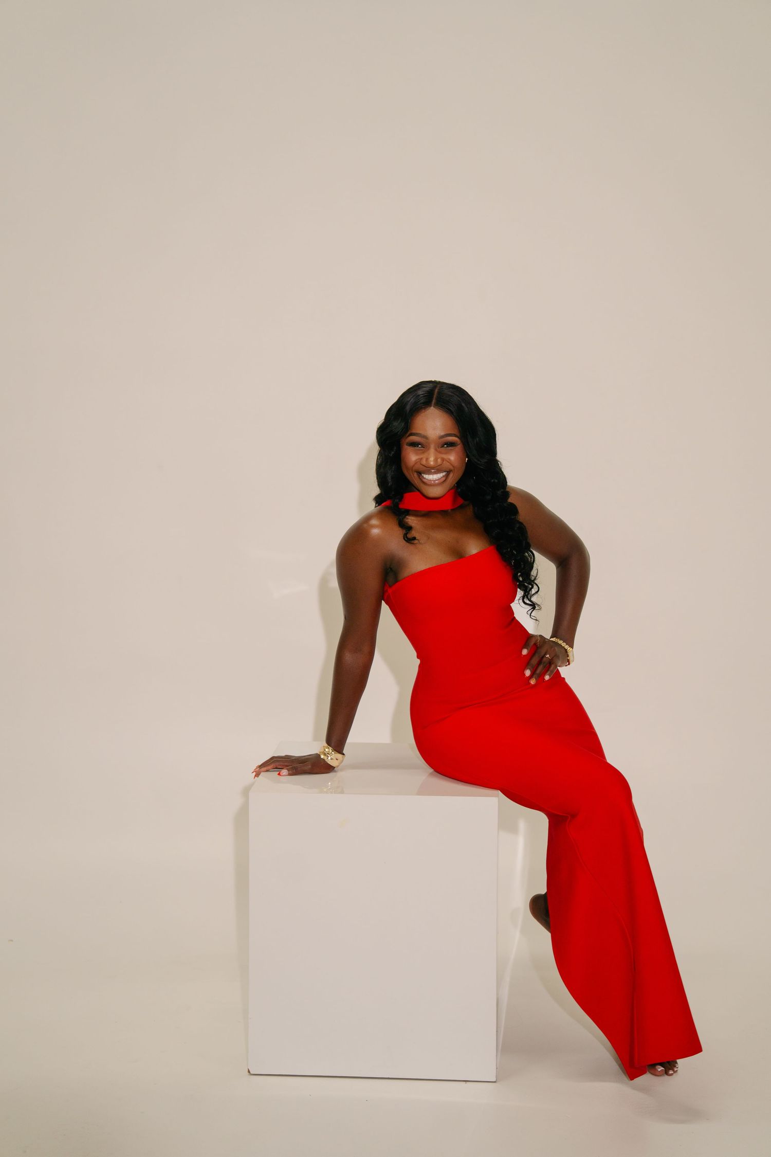 A person in a red dress poses dynamically with a white cube in a studio setting.