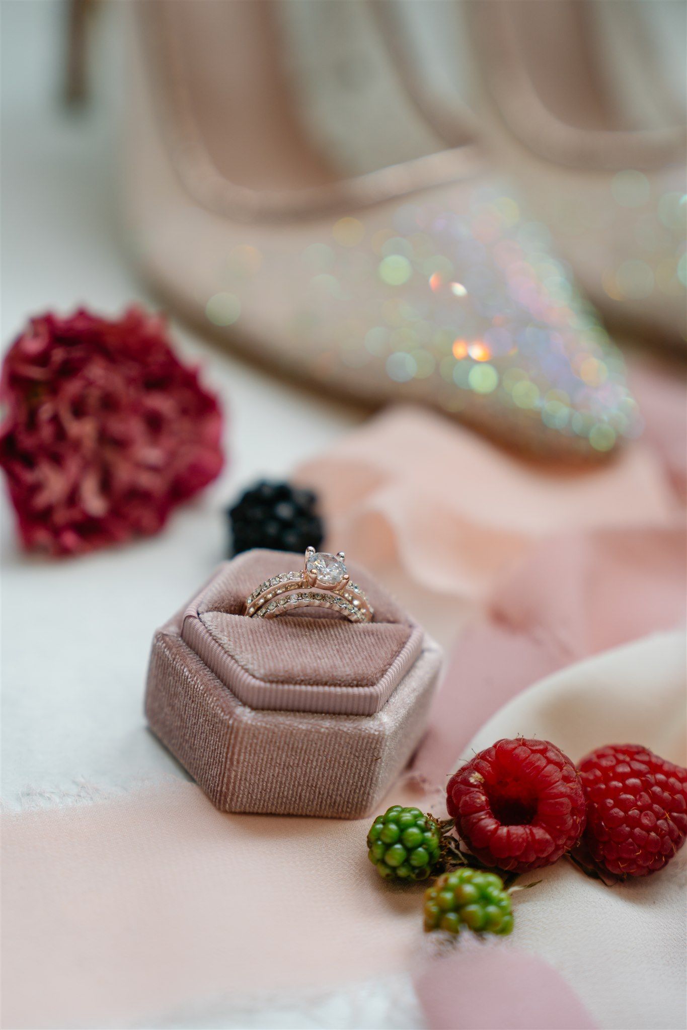 Close-up of engagement ring in velvet box with fresh berries and floral styling.