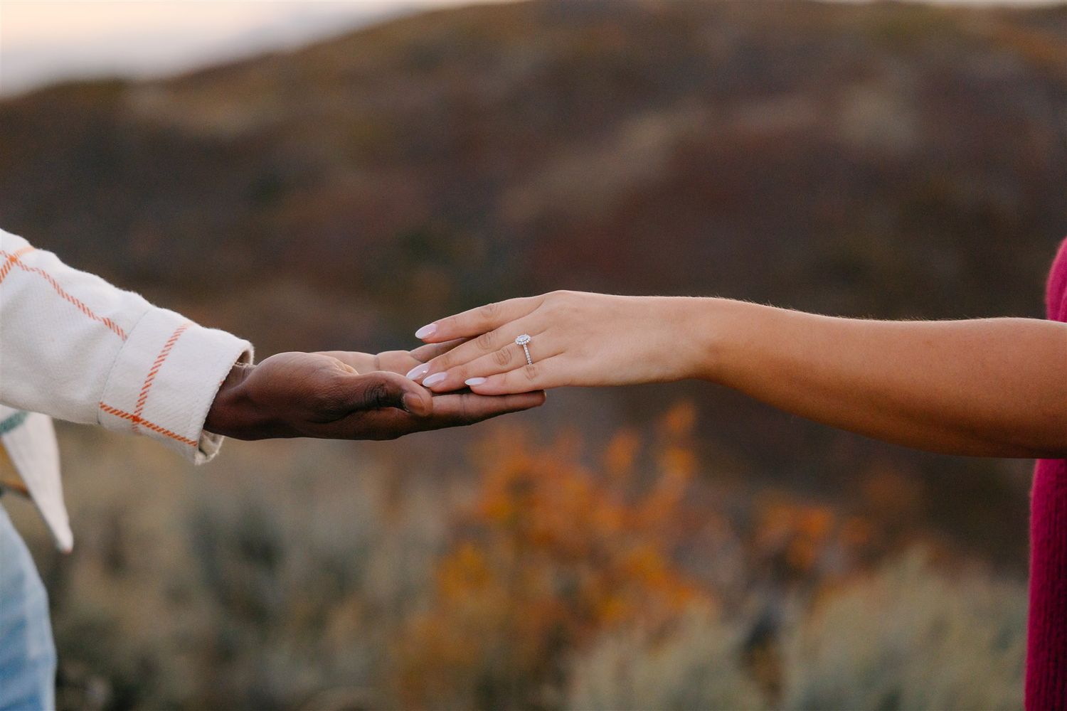 Detail shot of hands reaching toward each other against blurred outdoor background.