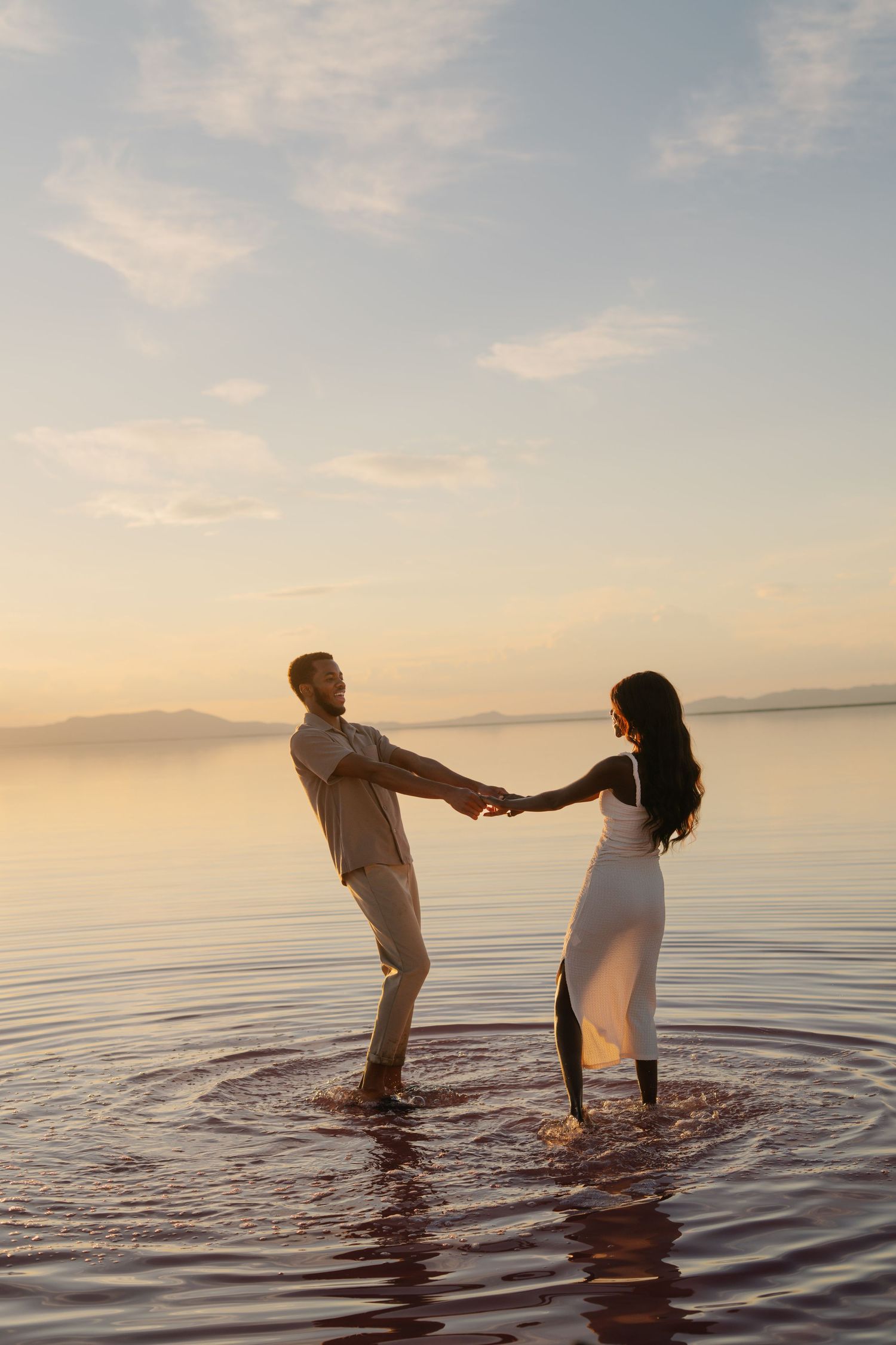 A couple creates circular ripples while dancing in tranquil waters at sunset.