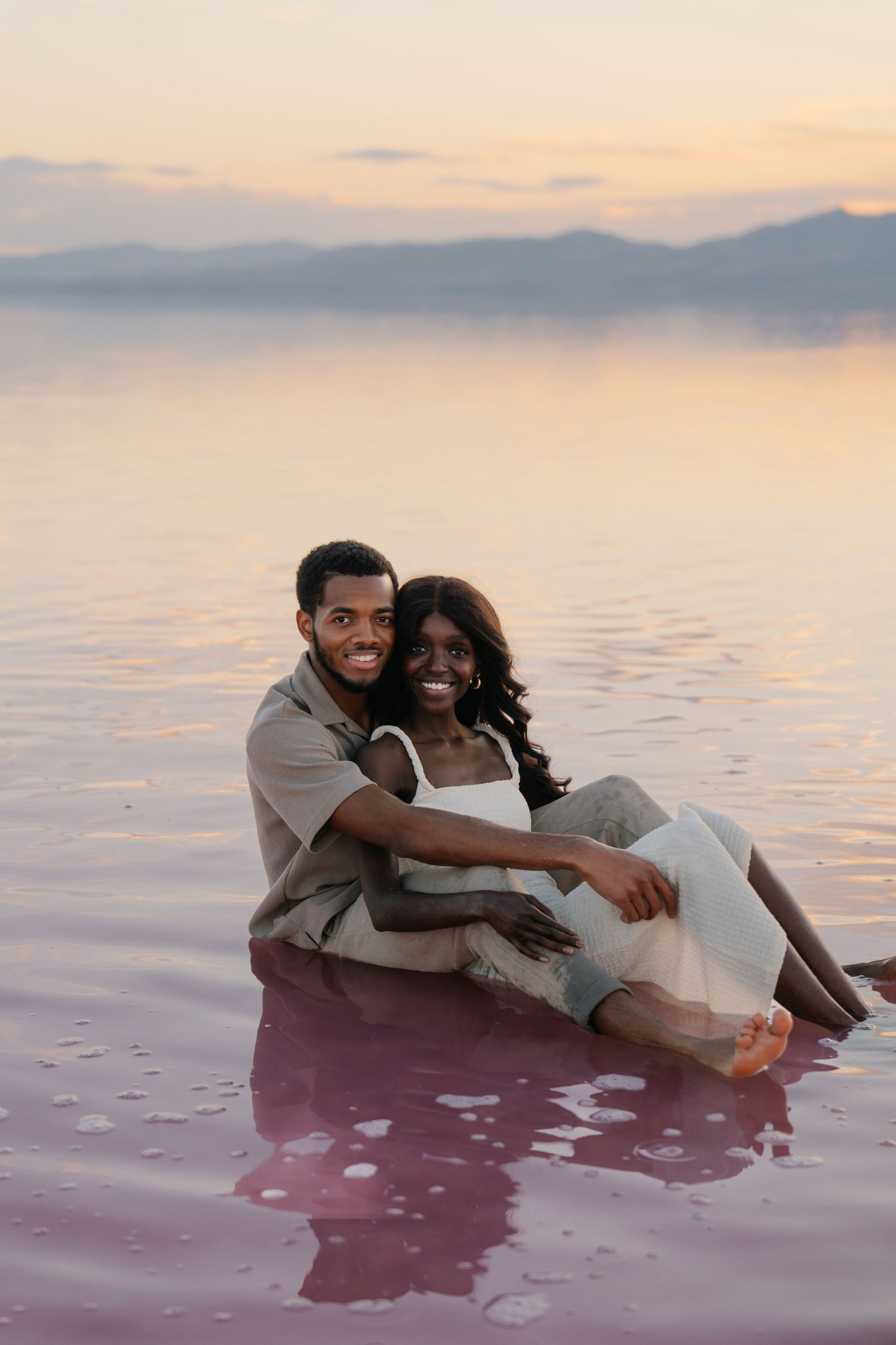 A couple relaxes together in pink salt waters during a dreamy sunset photoshoot.