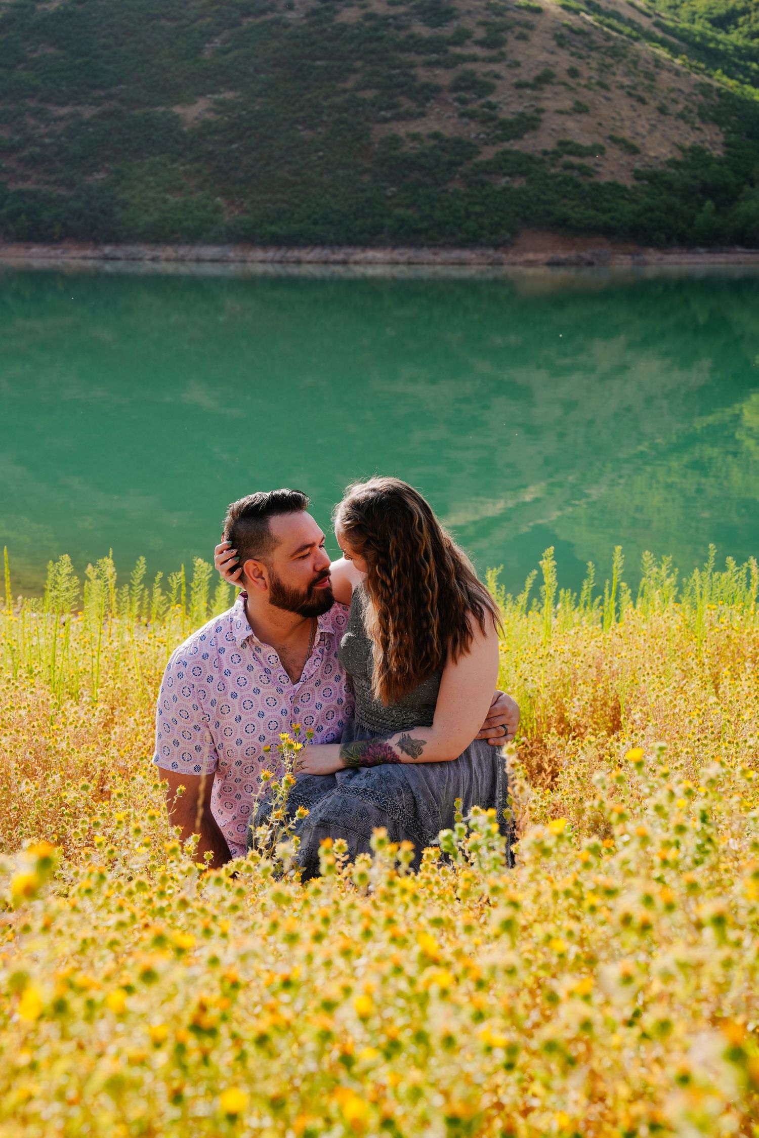 Couple embracing in a beautiful field of yellow wildflowers with mountains in the background.