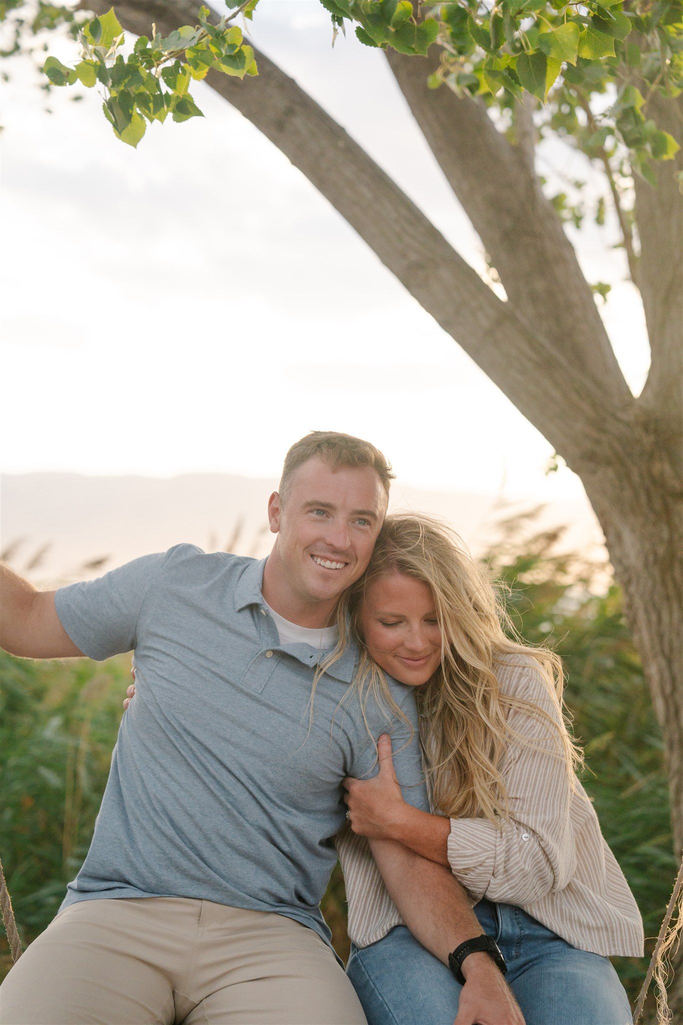 Couple shares intimate moments while sitting on a swing under a leafy tree.