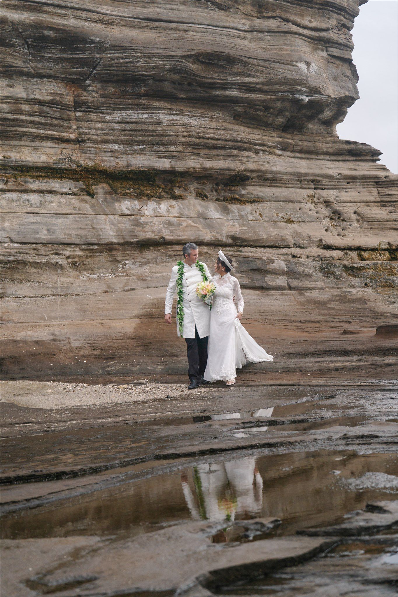 Couple taking wedding photos against dramatic rocky cliffs near a reflective pool.