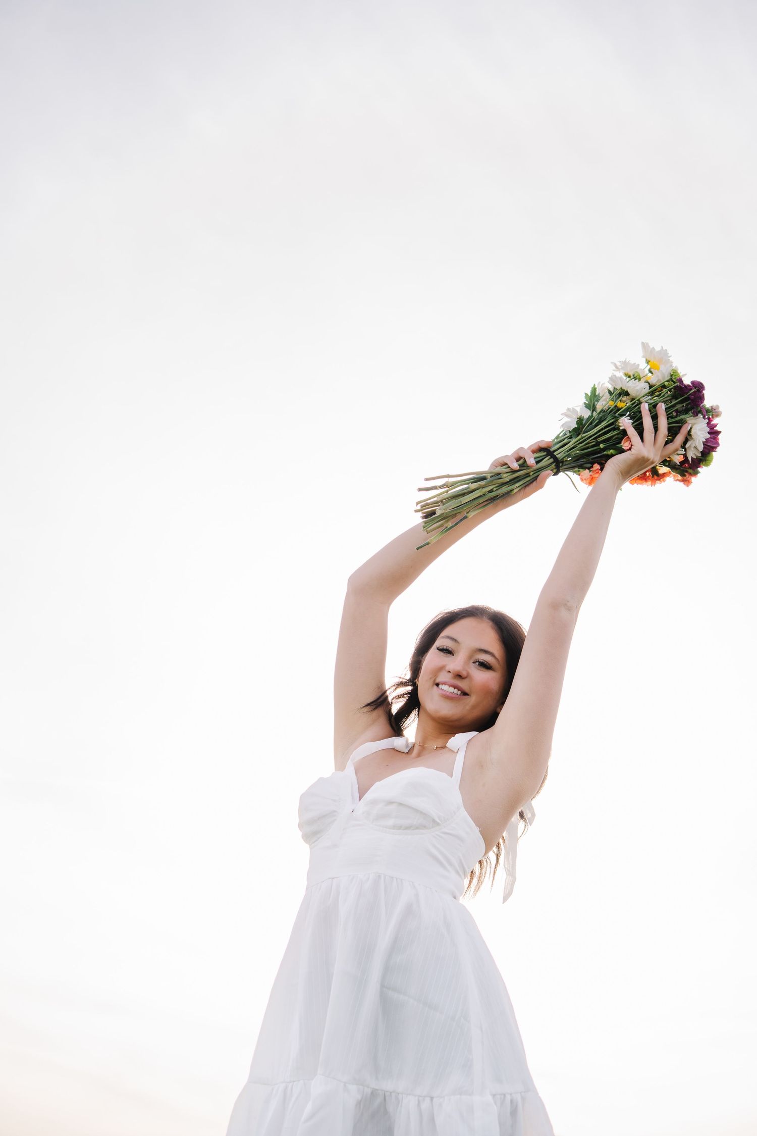 Person in white dress holding flowers overhead against white background.