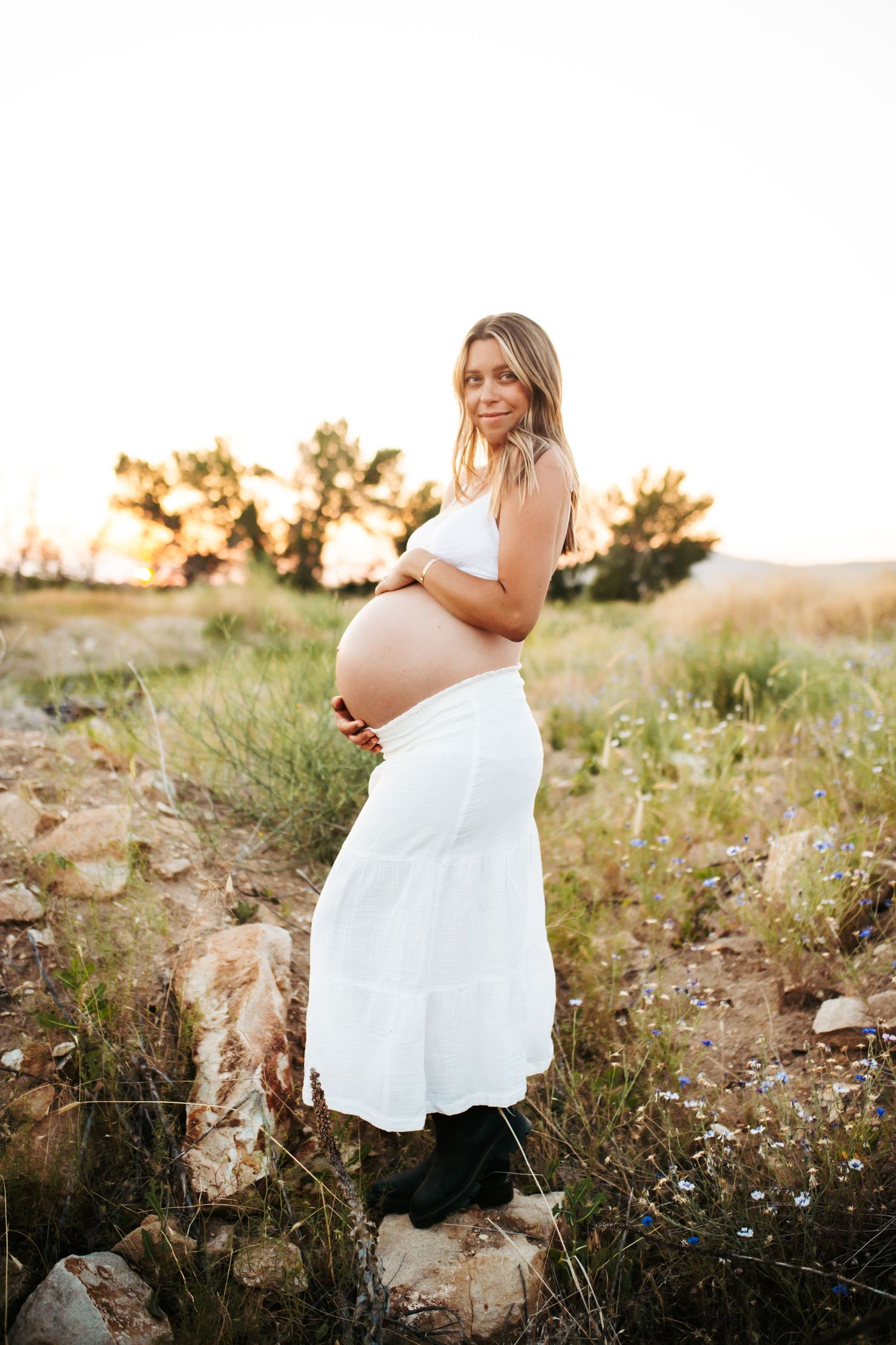 young woman holding her pregnant belly poses confidently for her maternity photos near Lucky Peak in Idaho