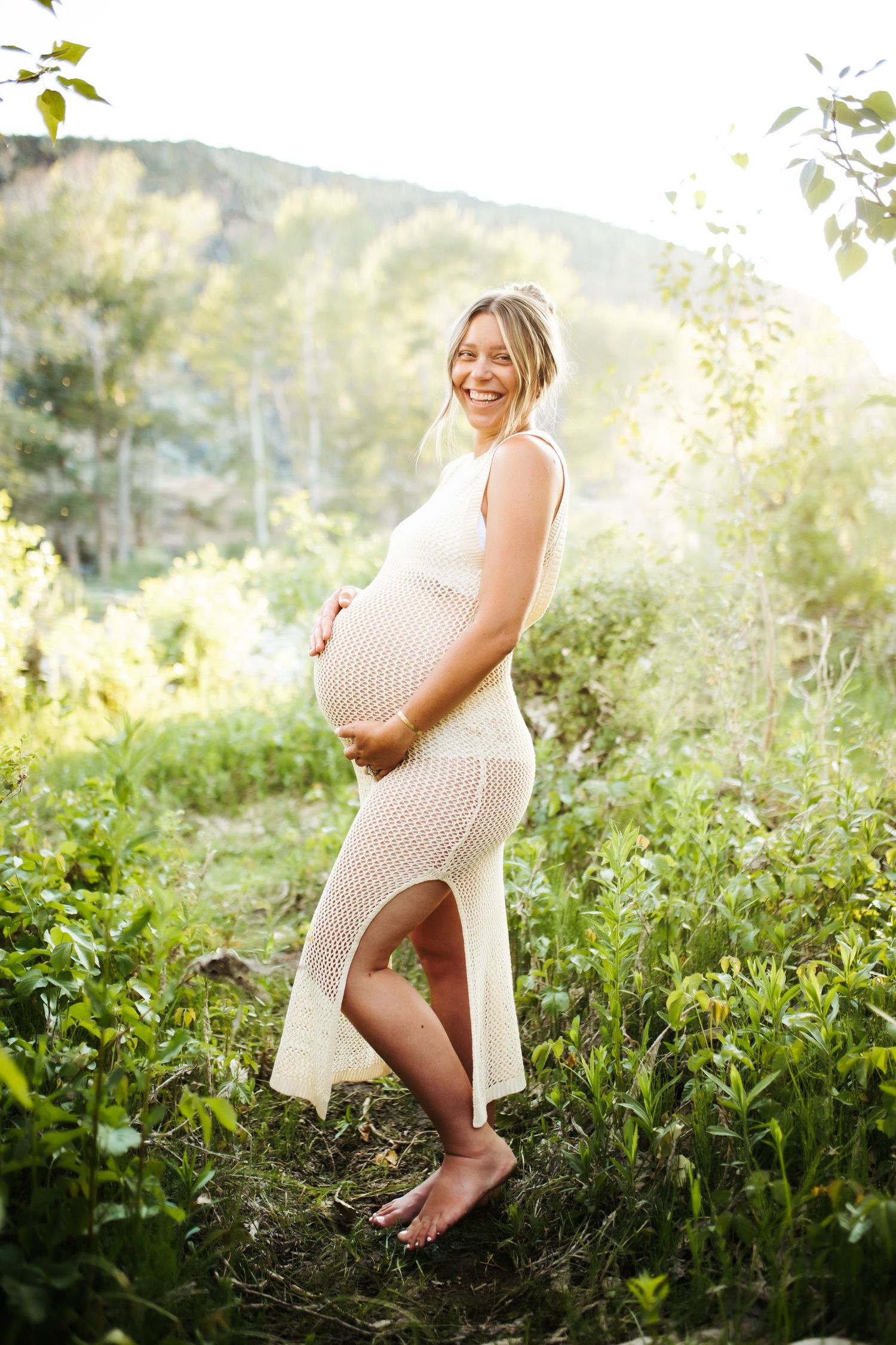 young woman holding her pregnant belly poses confidently for her maternity photos near Lucky Peak in Idaho